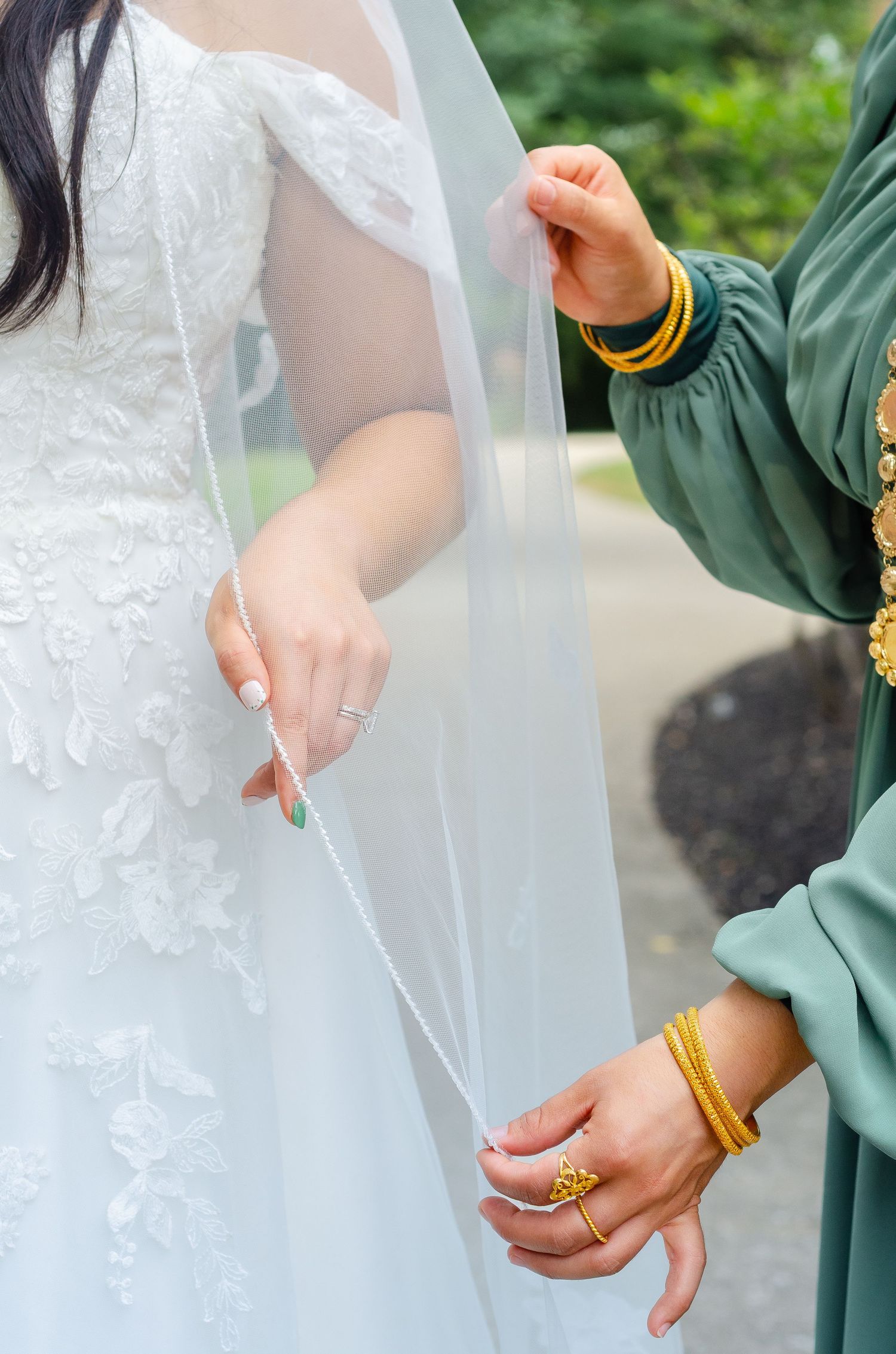 Close-up detail of hands adjusting a delicate white wedding veil with lace details and gold bracelets.