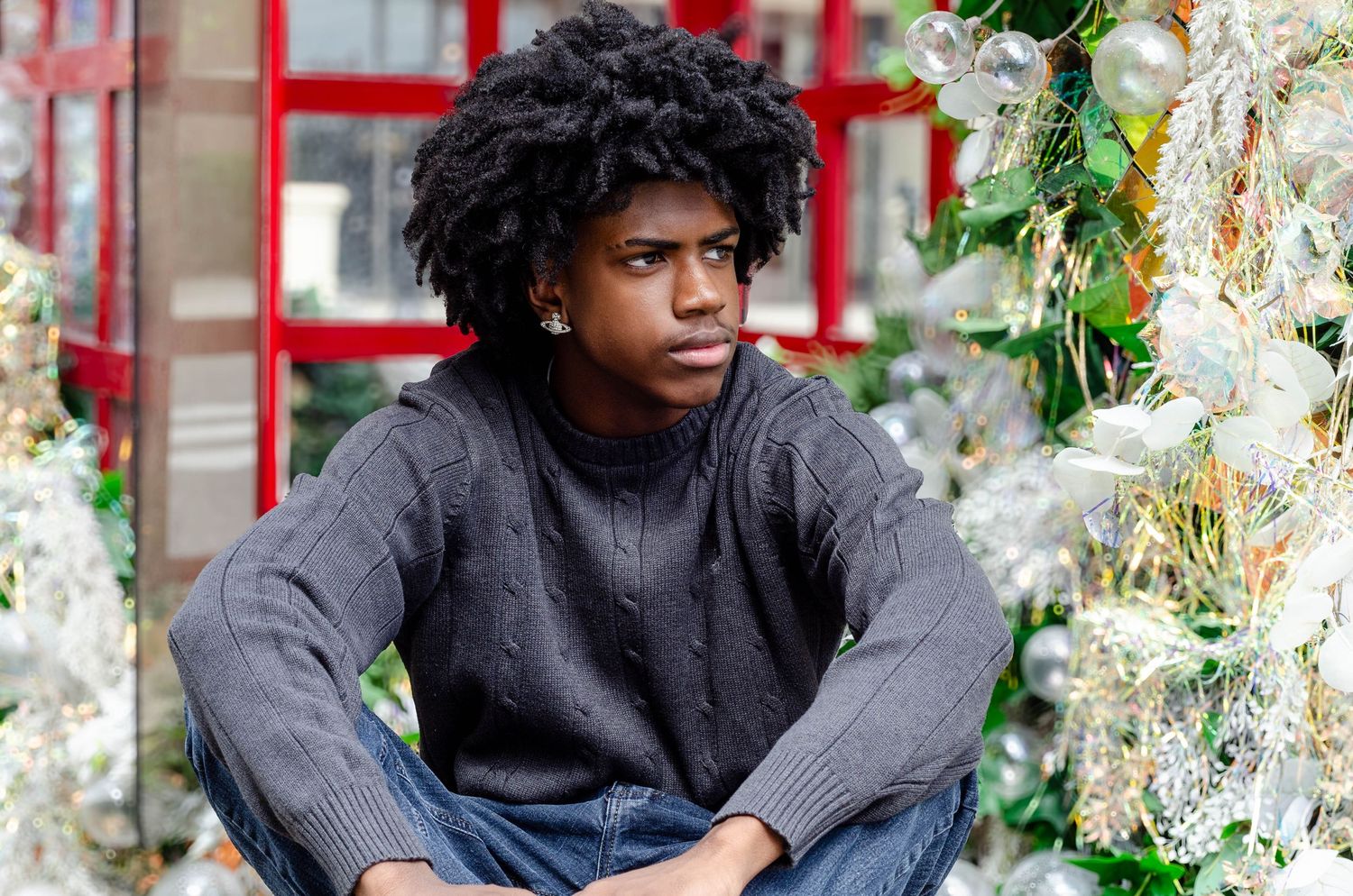 Person seated casually against a backdrop of white holiday decorations and red window frames.