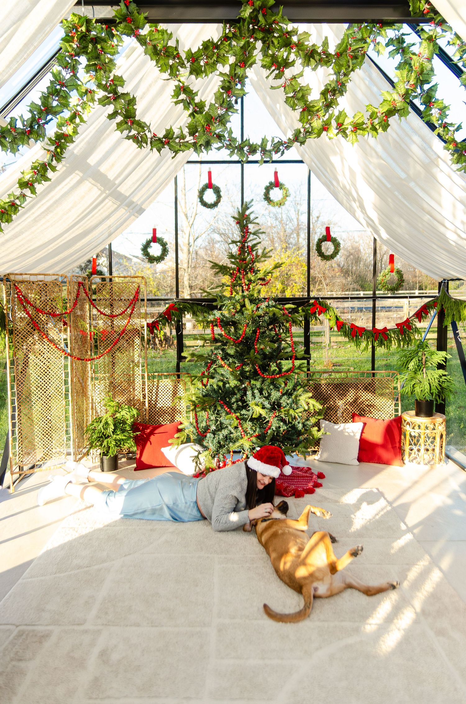 A festive sunroom decorated with Christmas wreaths and greenery features a dog lounging with owner. Photos by KM Conceptions Photograp