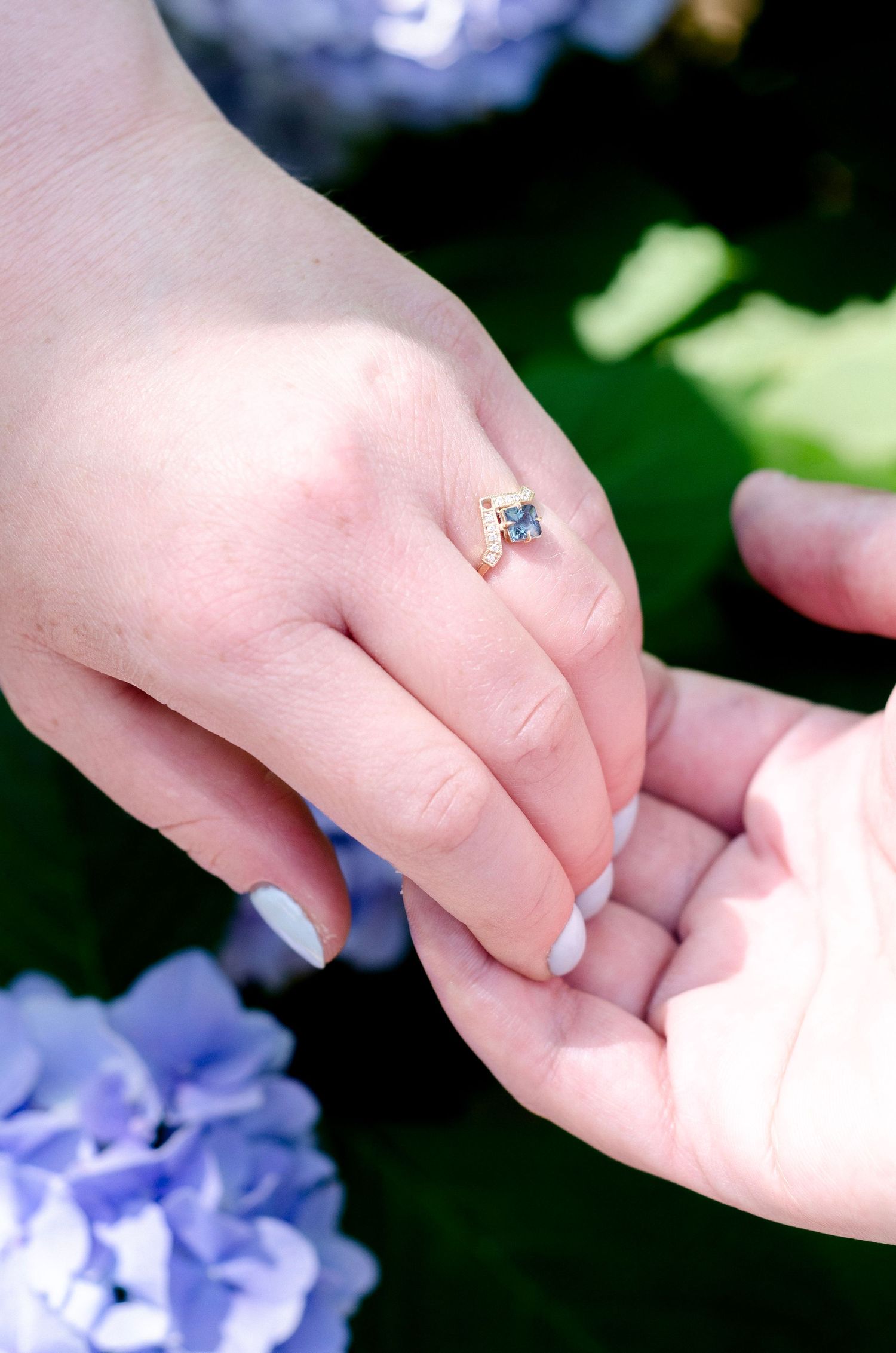 Close-up of hands with an engagement ring amid purple hydrangea flowers. Engagement photos by KM Conceptions Photography in New York.