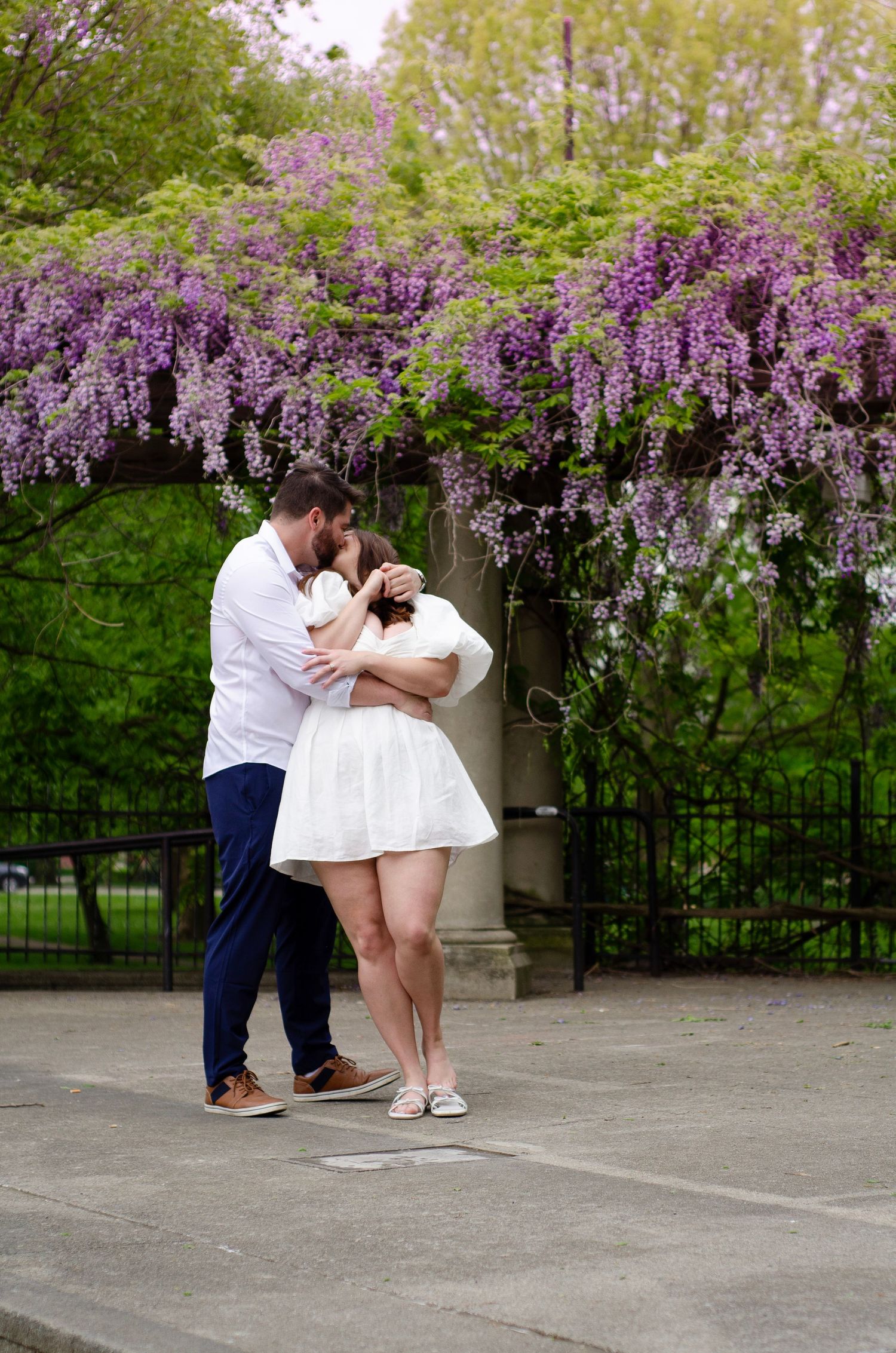 Romantic engagement photos under flowering wisteria in a spring garden setting.