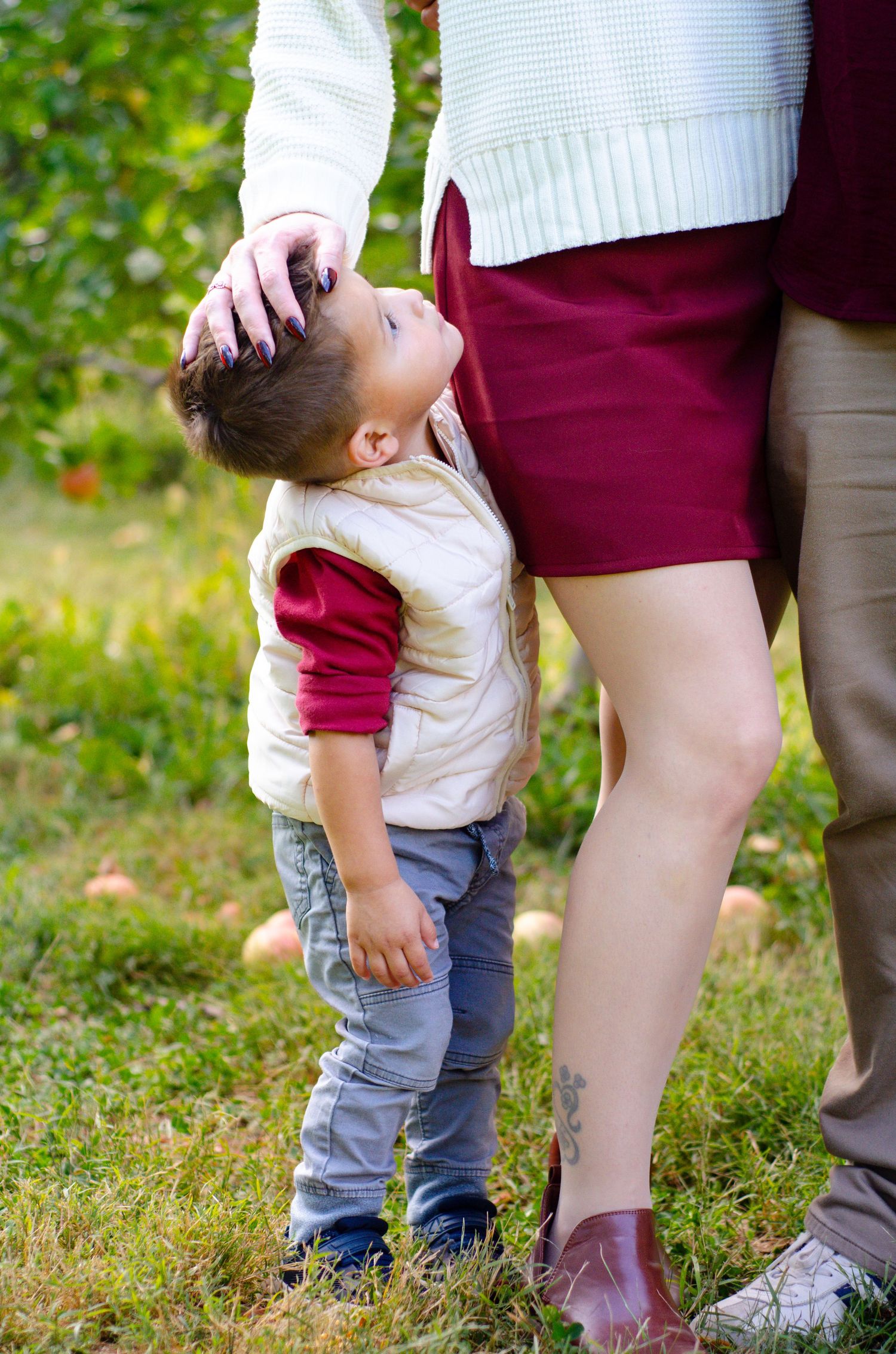 Small child in gray pants and white shirt walking near adult legs in an outdoor garden setting. Family photos by KM Conceptions Photography.