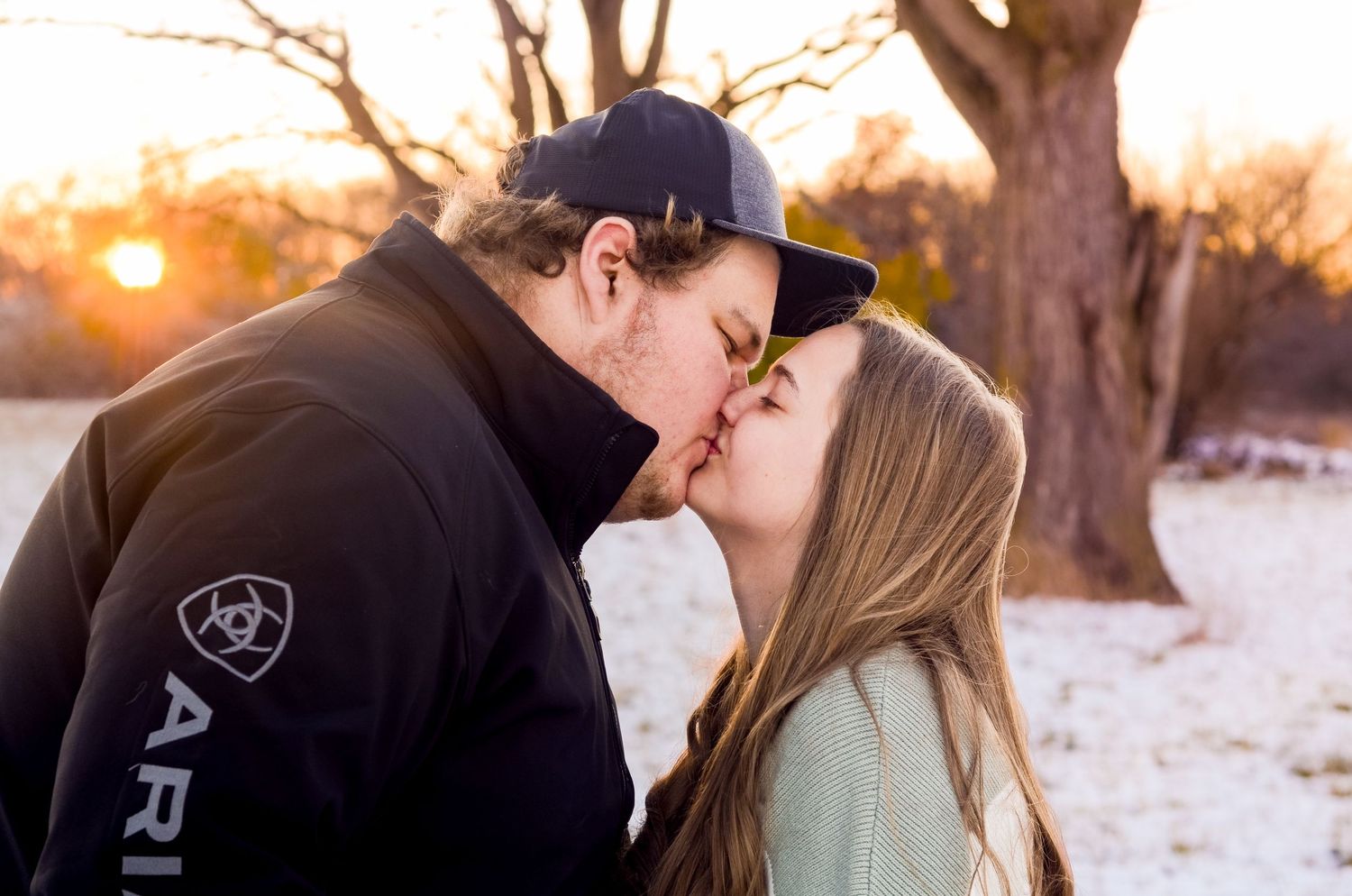 A romantic couple shares an intimate moment at sunset in a snowy winter landscape.
