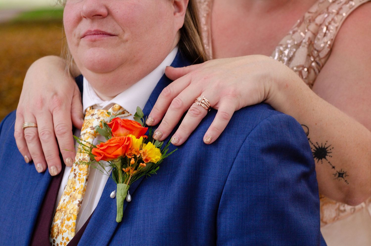 Close-up details of wedding attire showing a blue suit jacket with orange floral boutonniere. Photos by KM Conceptions Photography.