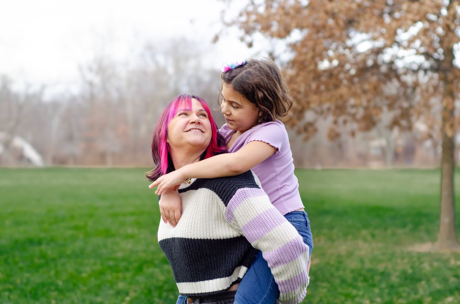 People embrace in a candid moment while standing on grass during fall.