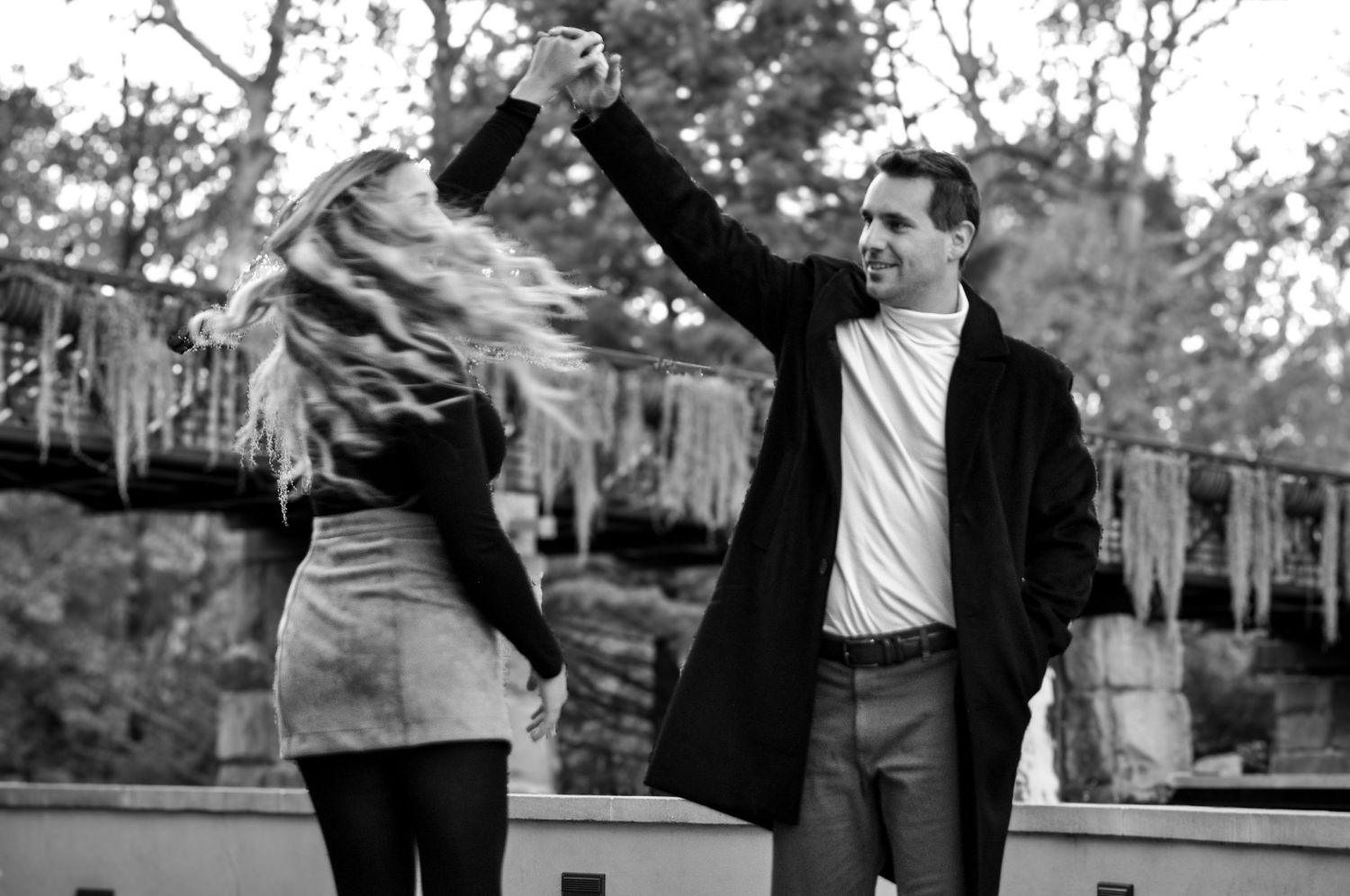 Black and white photo of couple dancing outdoors with dramatic movement and joy.