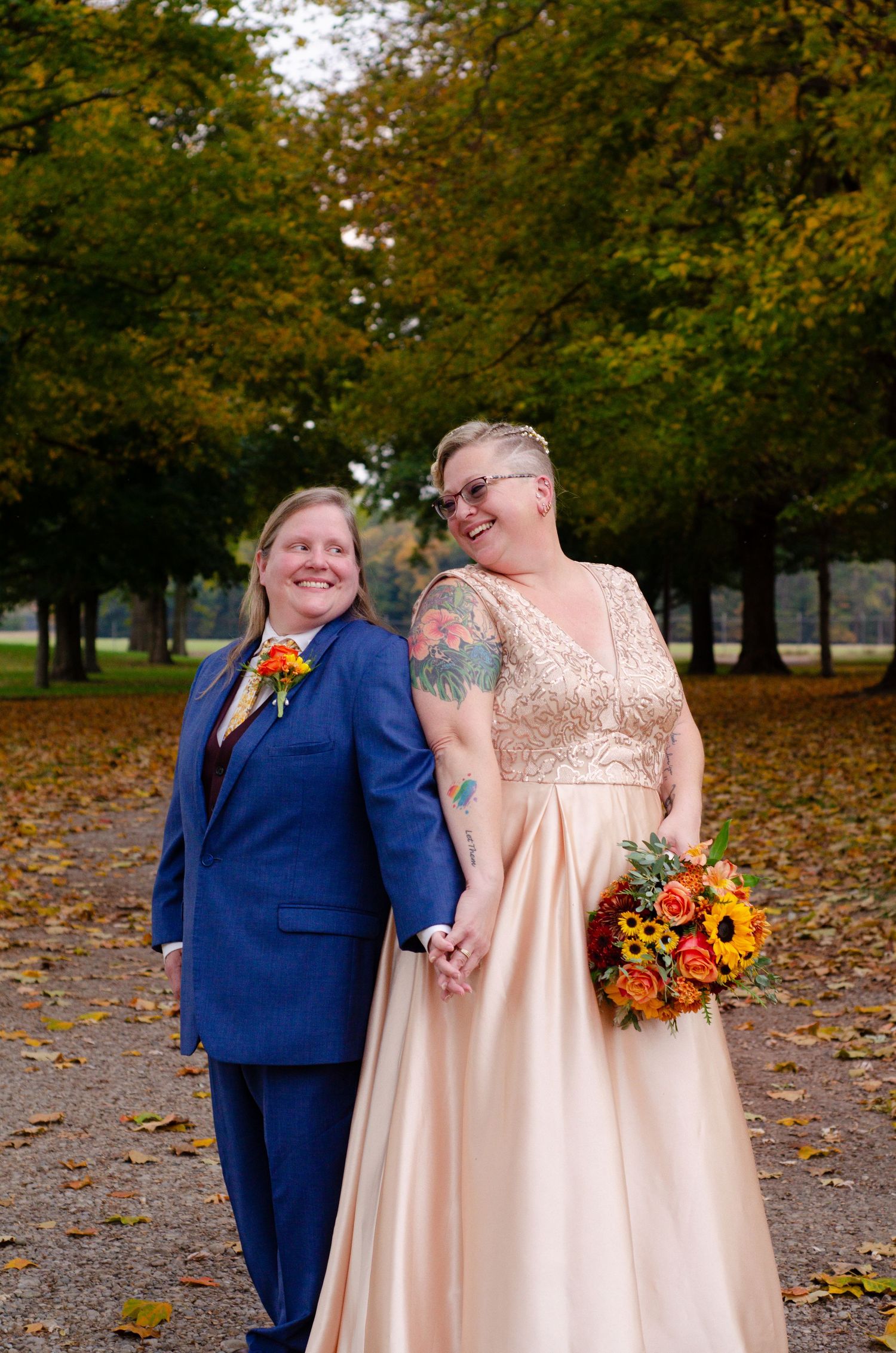 A wedding couple poses in a park with fallen autumn leaves, wearing navy blue and blush formal attire. Photos by KM Conceptions Photography.