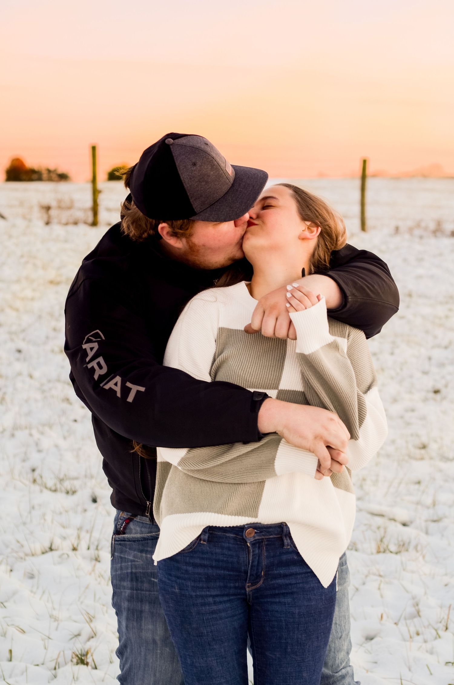 Two people share an intimate moment in casual winter clothing against a snowy landscape.