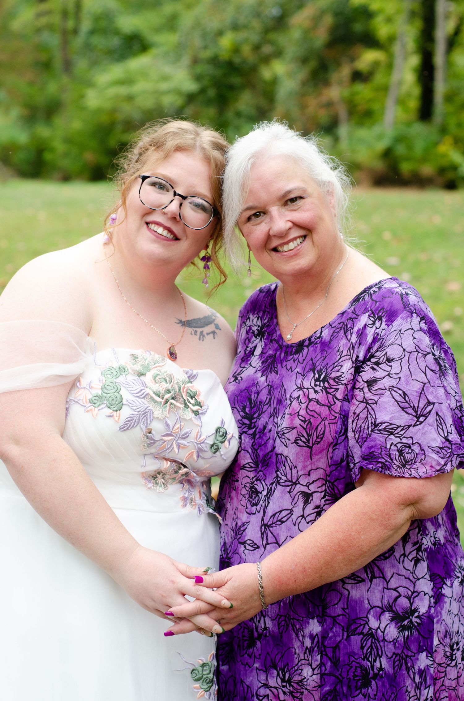 Wedding portrait featuring a white dress and vibrant purple floral pattern dress in an outdoor setting. Family photos by KM Conceptions.