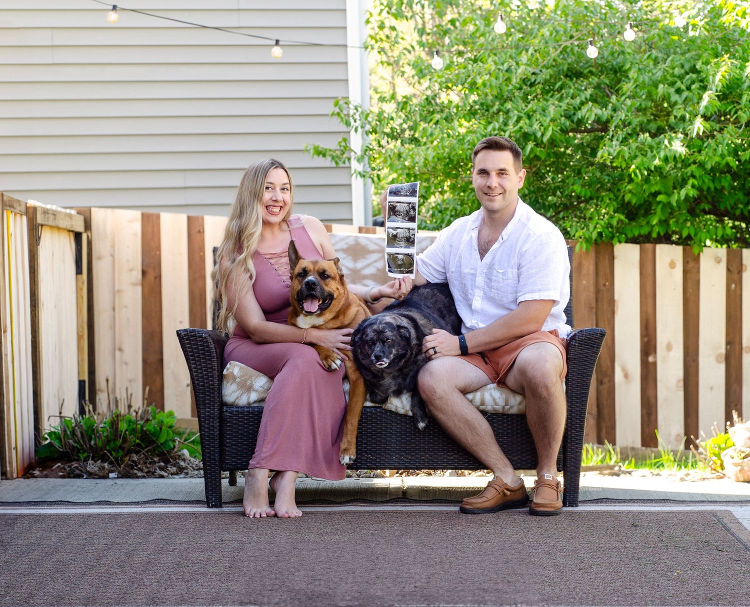 A family relaxes on their backyard patio with wooden fence and string lights visible.