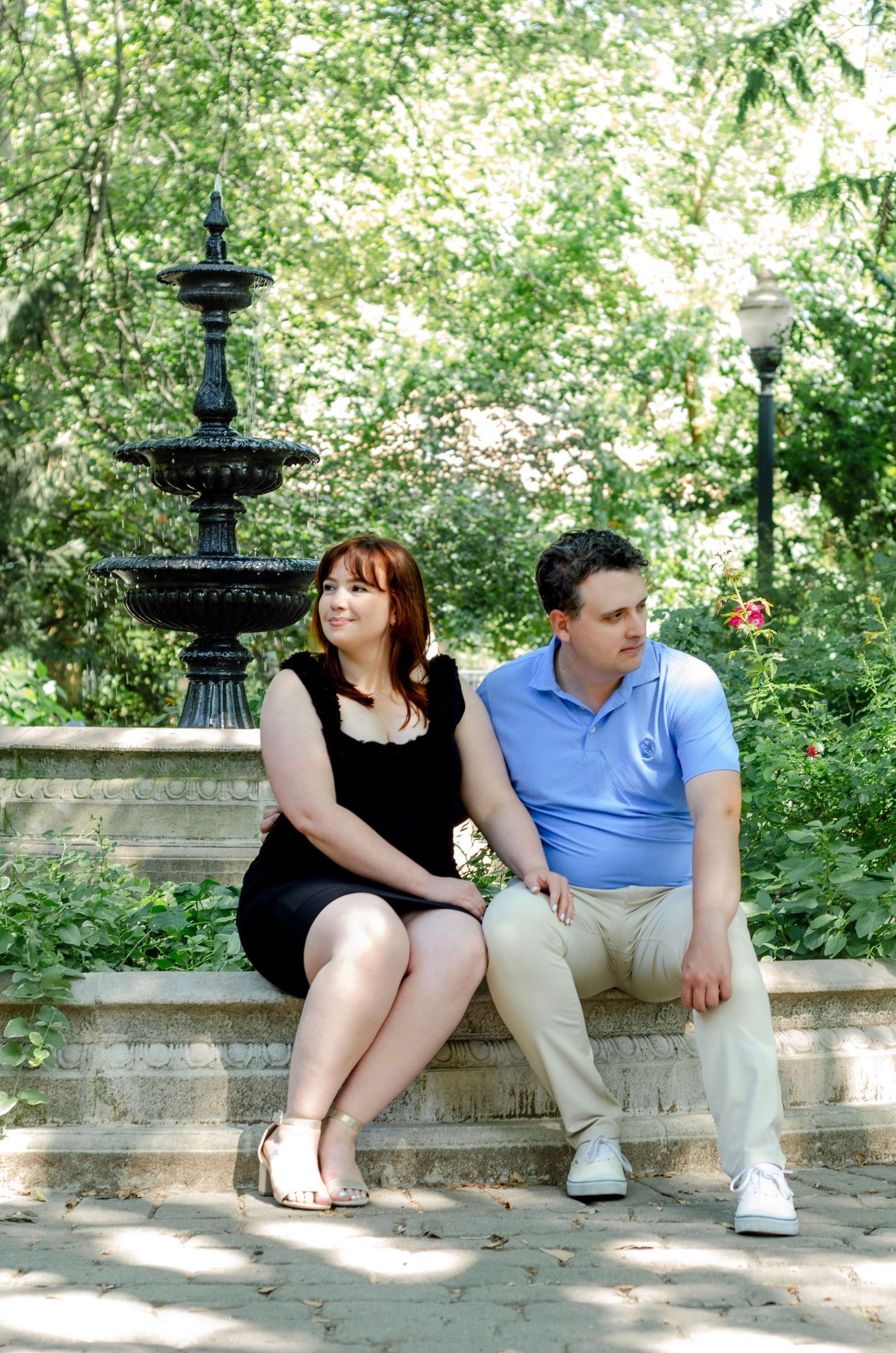 Couple relaxing on stone bench near decorative fountain in park. Engagement photos by KM Conceptions Photography in New York.