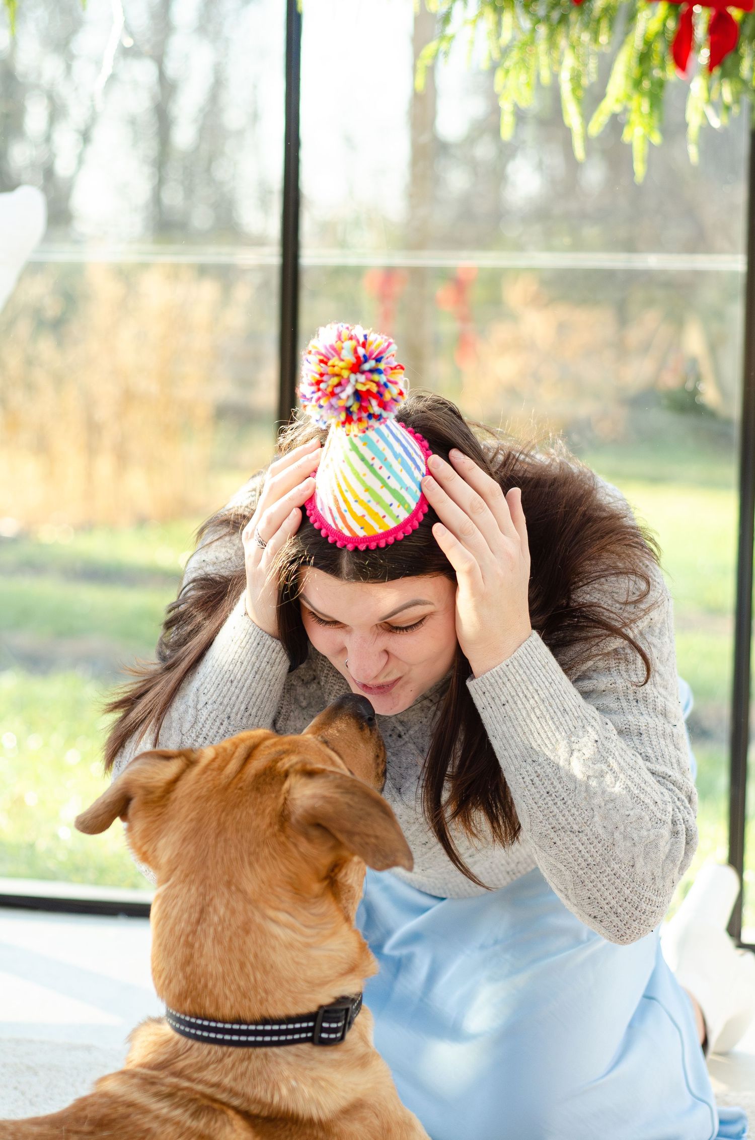 Dog and companion share playful moment wearing winter hats in bright sunroom. Photos by KM Conceptions Photography.