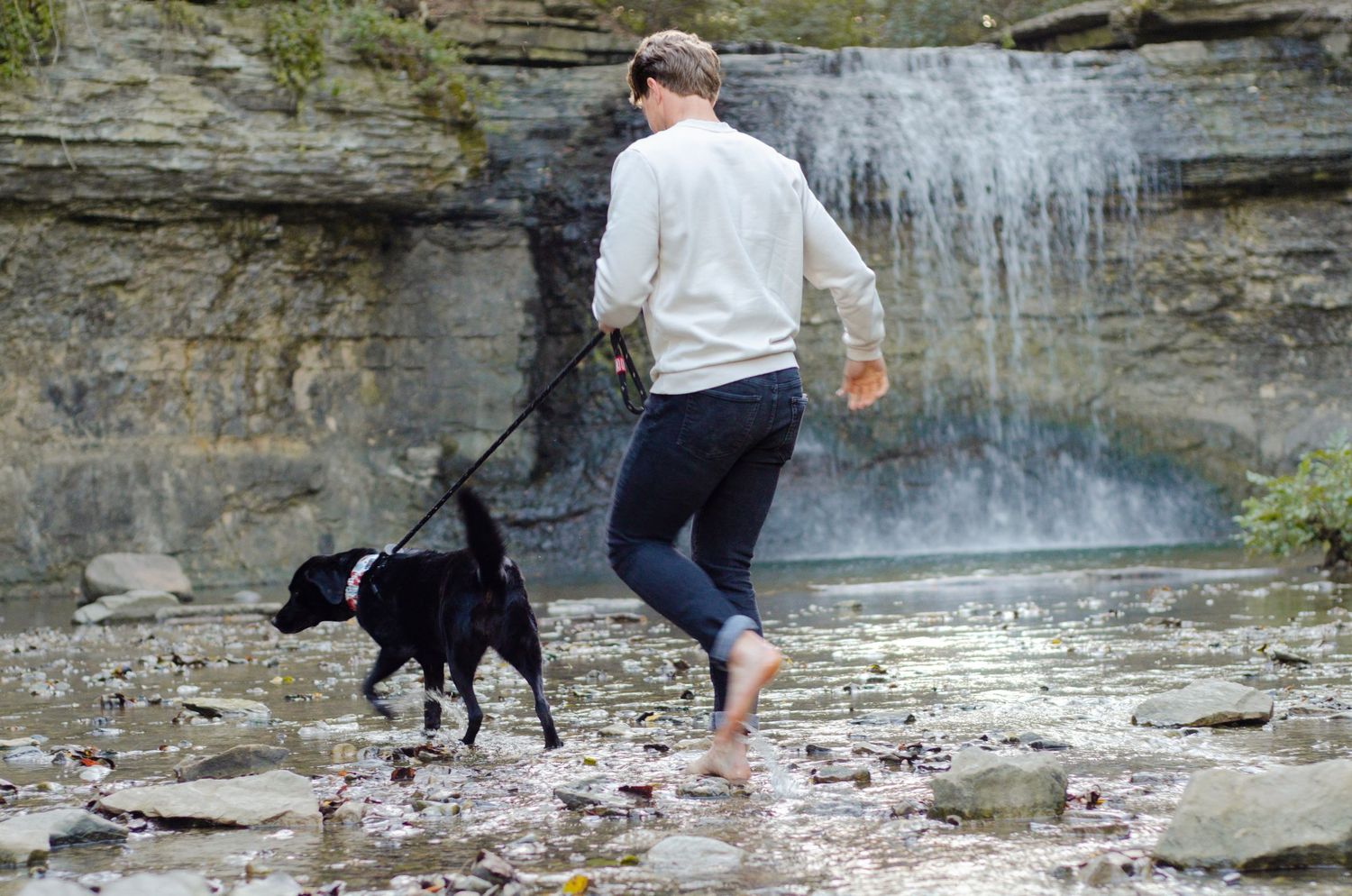 A couple and their black dog explore a scenic waterfall area with rocky terrain. Pet photos by KM Conceptions Photography in Columbus, OH.