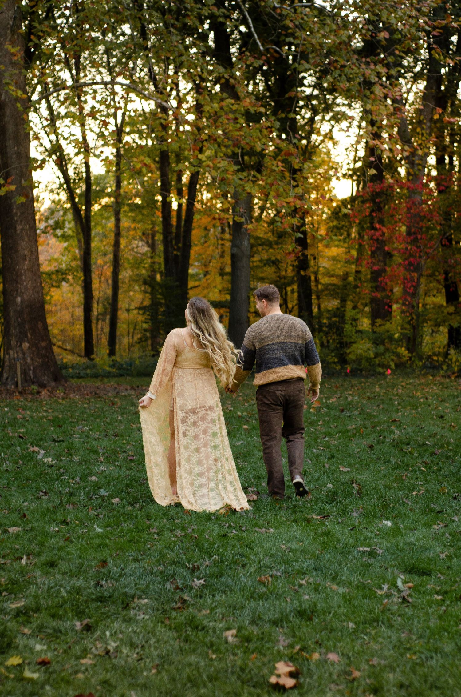 Couple walks through a grassy hillside with golden autumn trees in background. Maternity photos by KM Conceptions Photography in Columbus, O