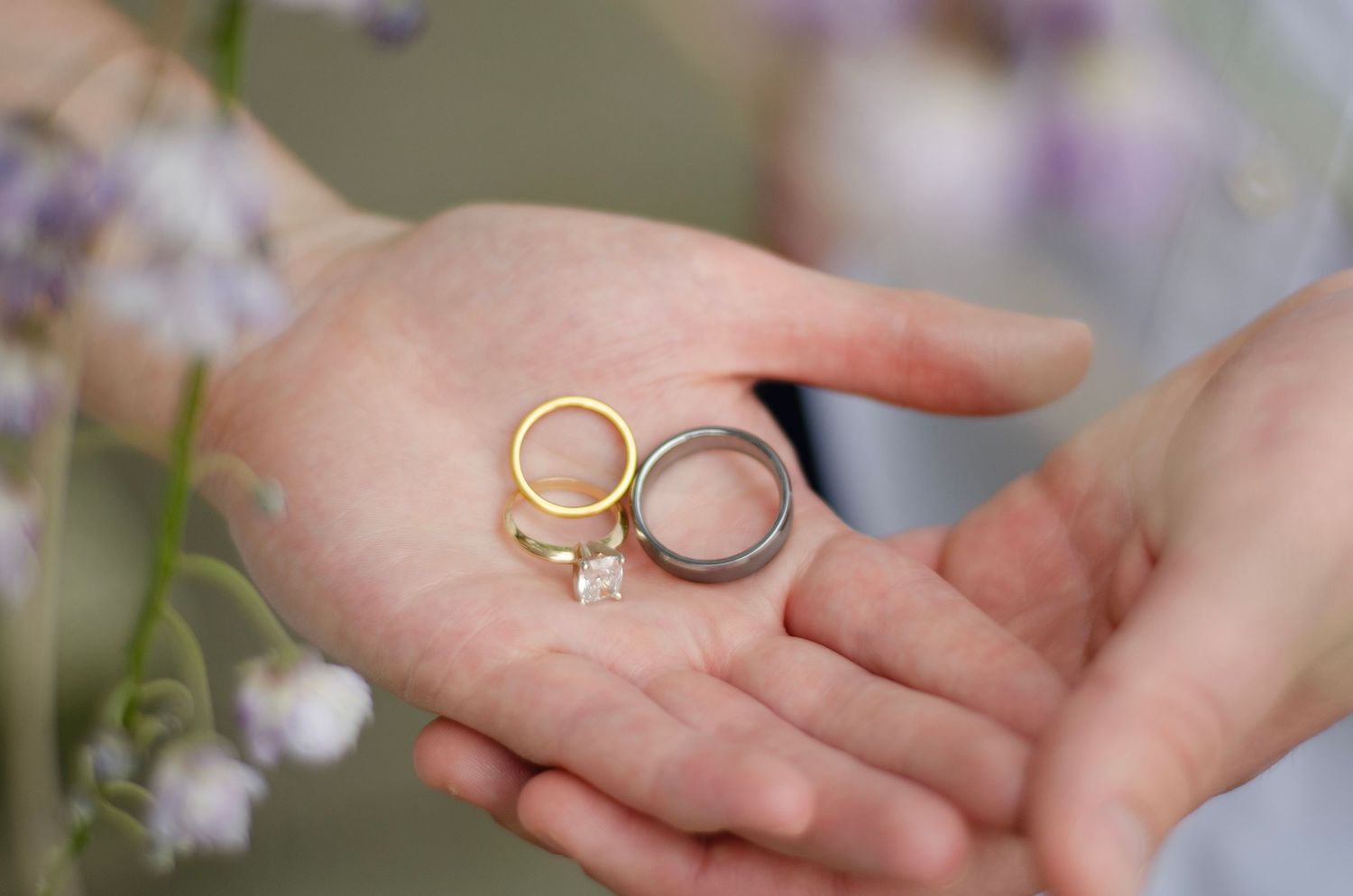 Close-up shots of hands exchanging wedding rings during a romantic ceremony with delicate white flowers in the background. KM Conceptions