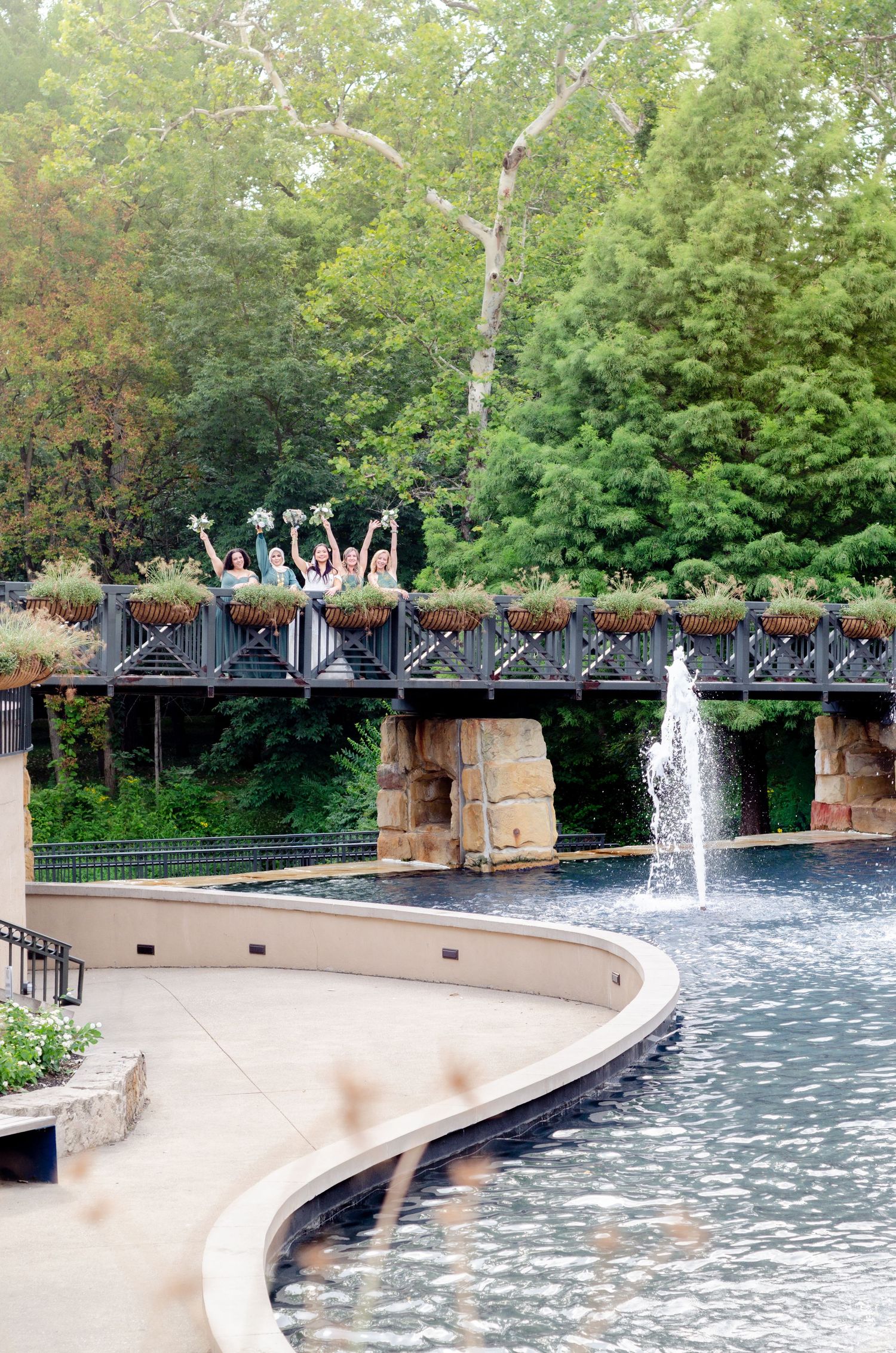 A curved fountain wall with water features and stone pillars creates a peaceful scene in a lush green park setting.