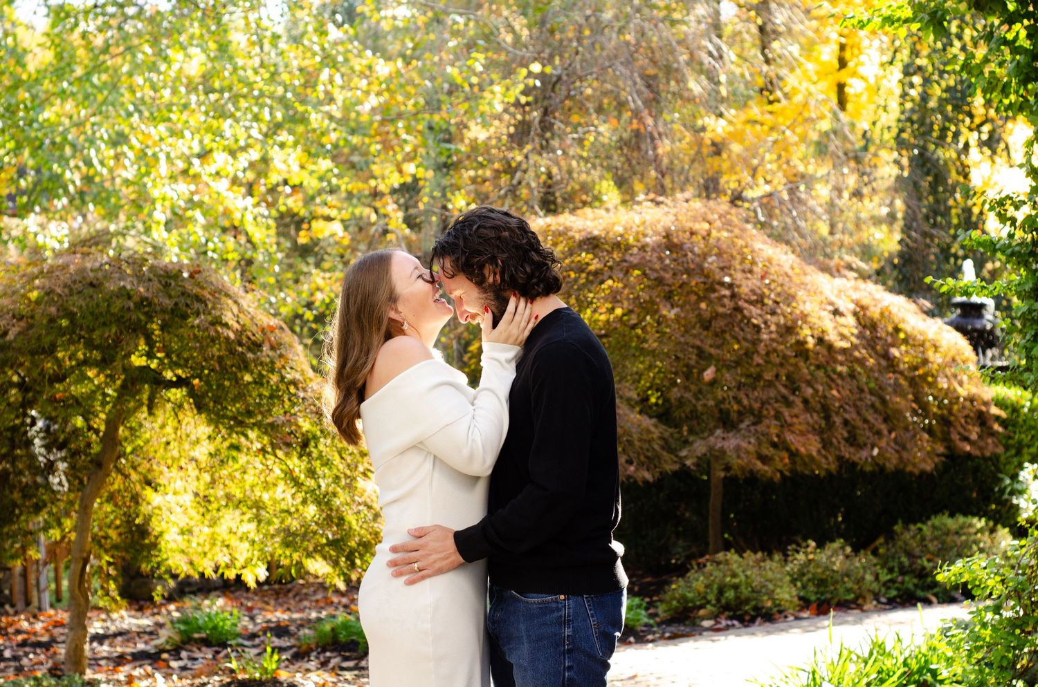 Couple sharing a romantic moment in a sunlit autumn garden with colorful foliage.
