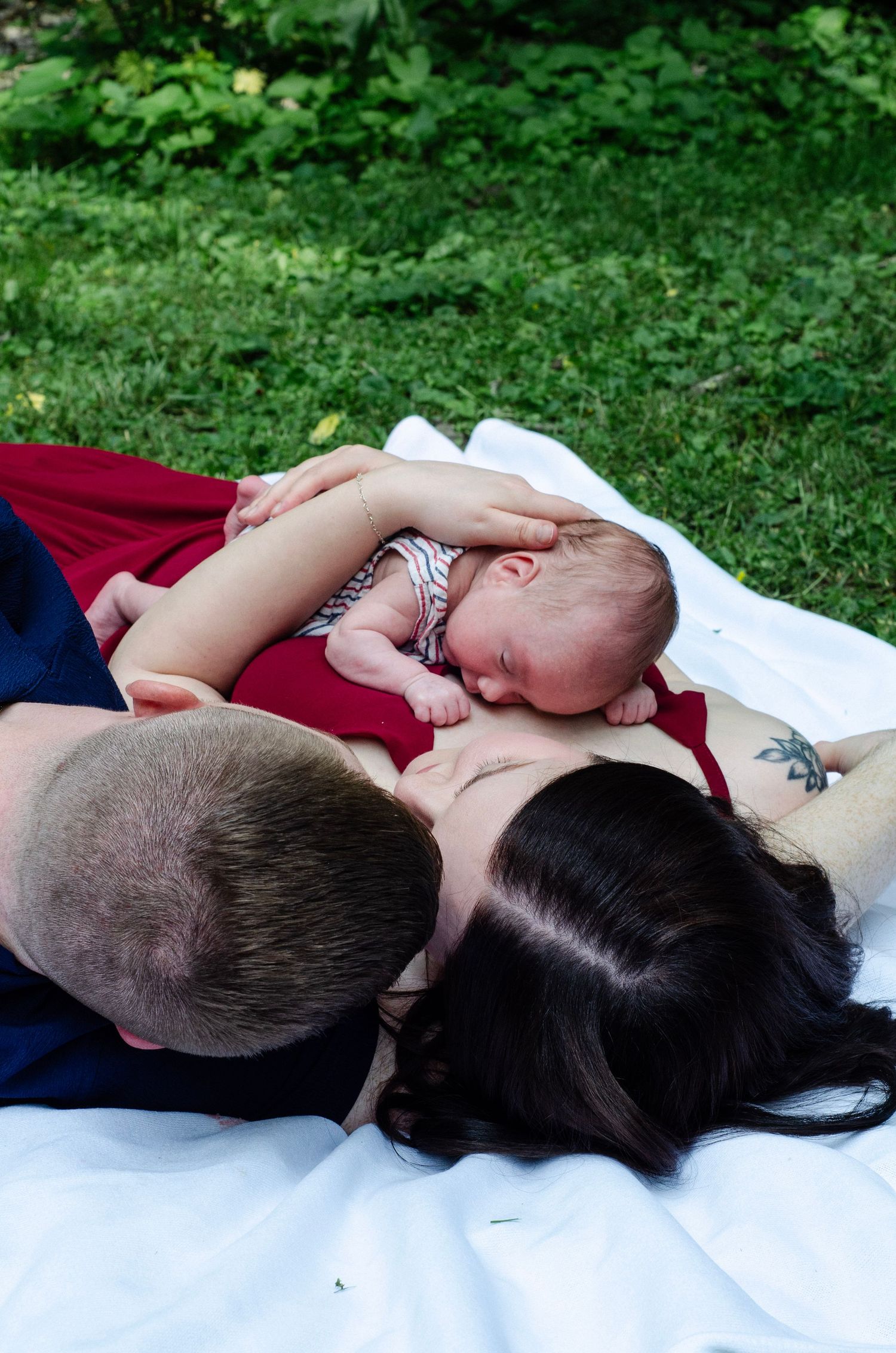 A peaceful family moment on a white blanket in a green garden setting. Newborn photos by KM Conceptions Photography in Columbus, OH.