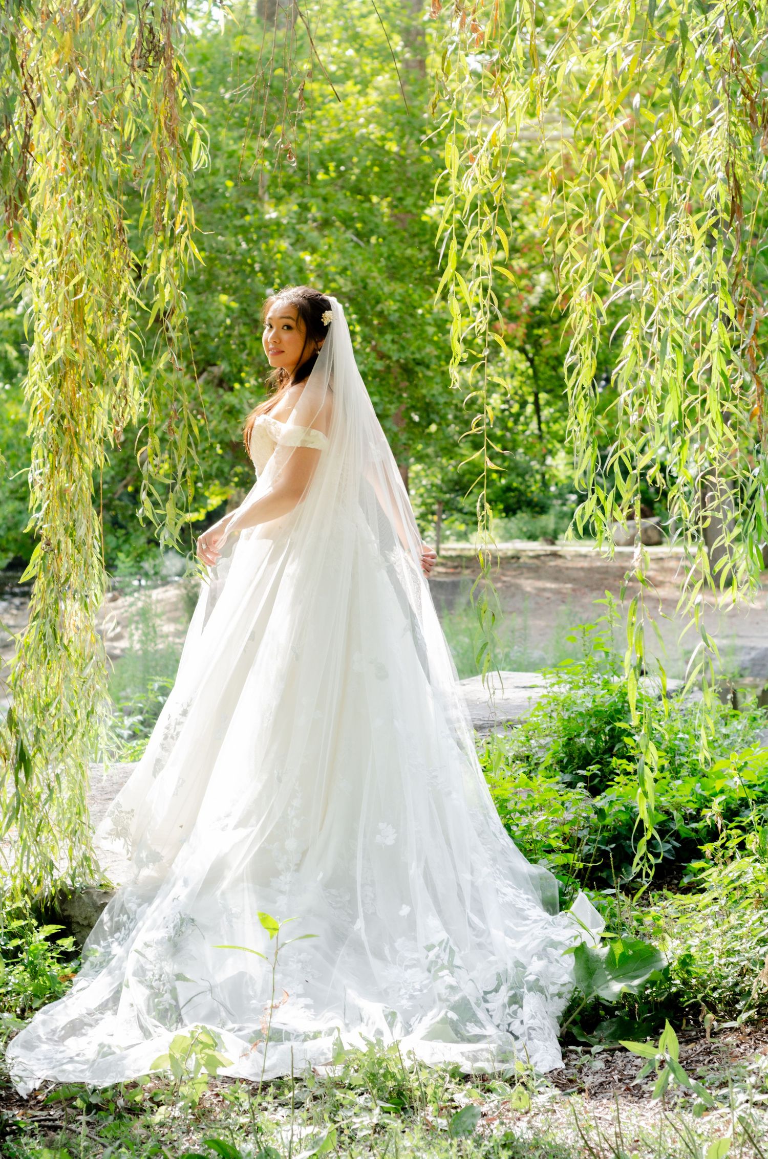 Elegant bride in flowing white gown poses under weeping willow trees. Wedding photos by KM Conceptions Photography in Columbus, OH