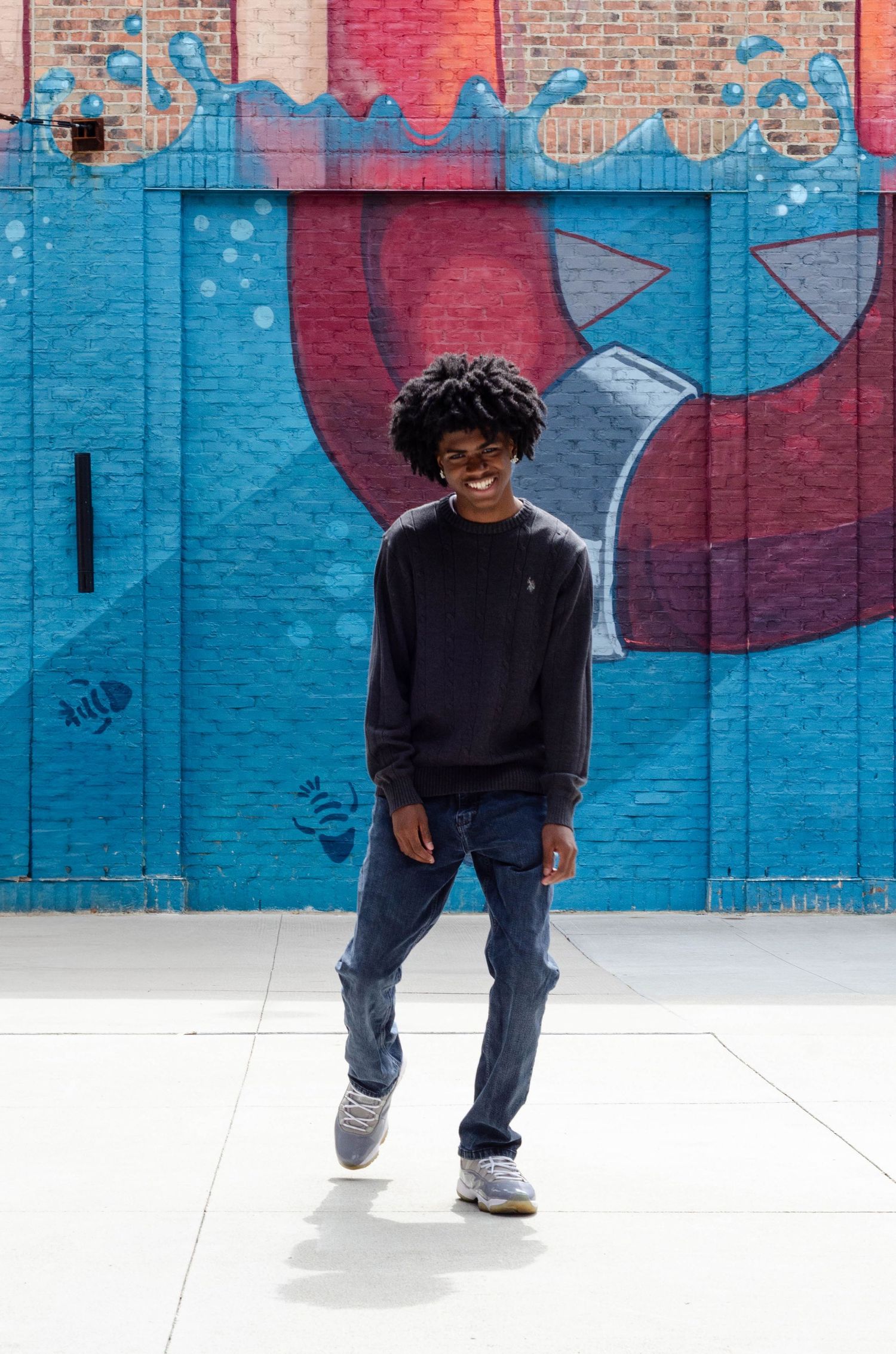 Person in black clothing dances in front of a vibrant blue and red graffiti wall.