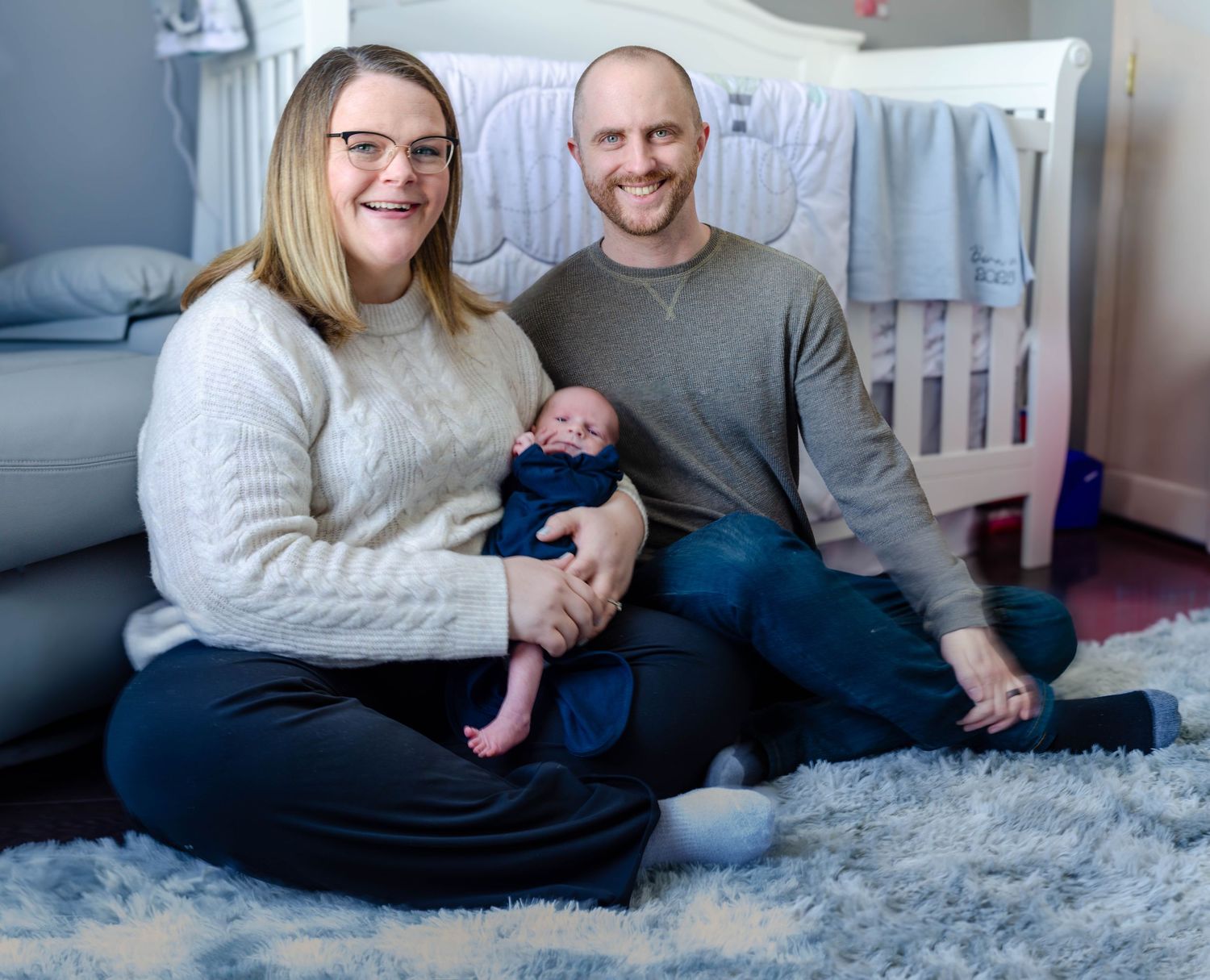 A family sits together on a soft gray carpet in a cozy indoor setting. Newborn photos by KM Conceptions Photography in Columbus