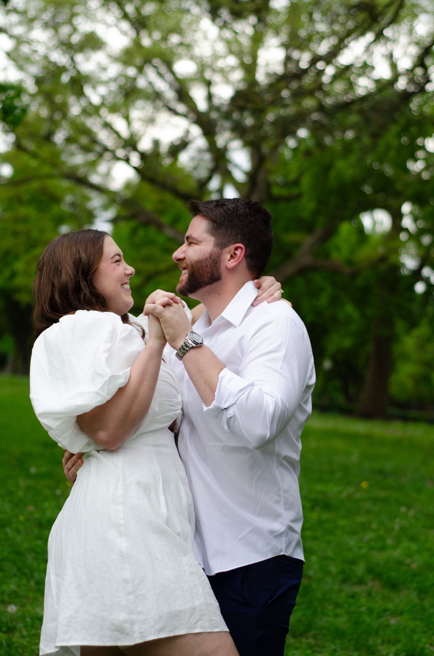 Couple in coordinated white outfits sharing lighthearted moments in a park.