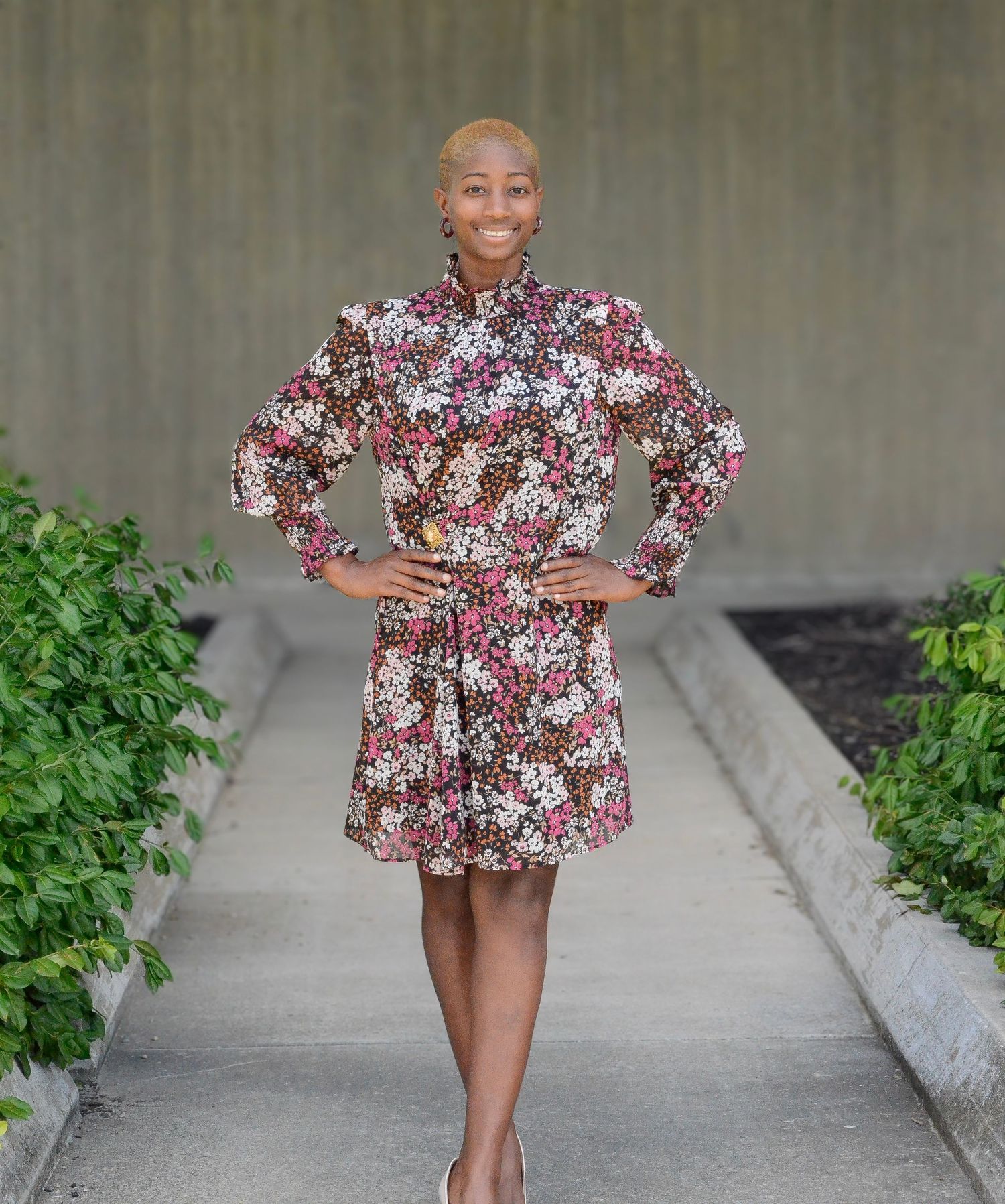 Person in floral print dress posing confidently on concrete walkway.
