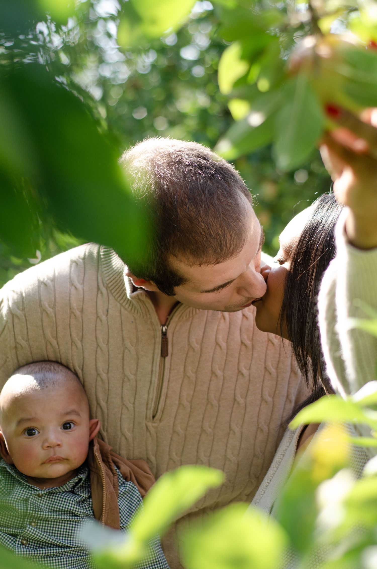 A tender family moment captured through green leaves in natural sunlight. Family photos by KM Conceptions Photography in Columbus, OH.