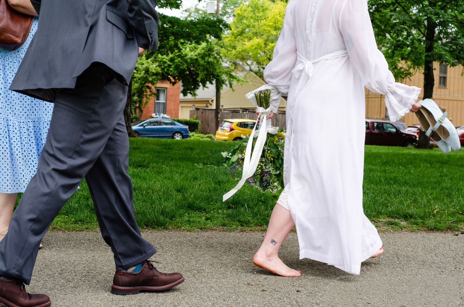 People's feet and legs walking in a line on a paved path beside a grassy area during an outdoor event.