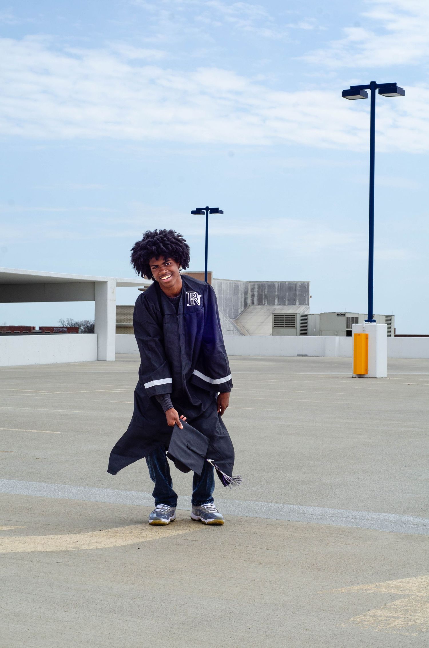Graduate in dark jacket poses with diploma on empty rooftop parking deck.
