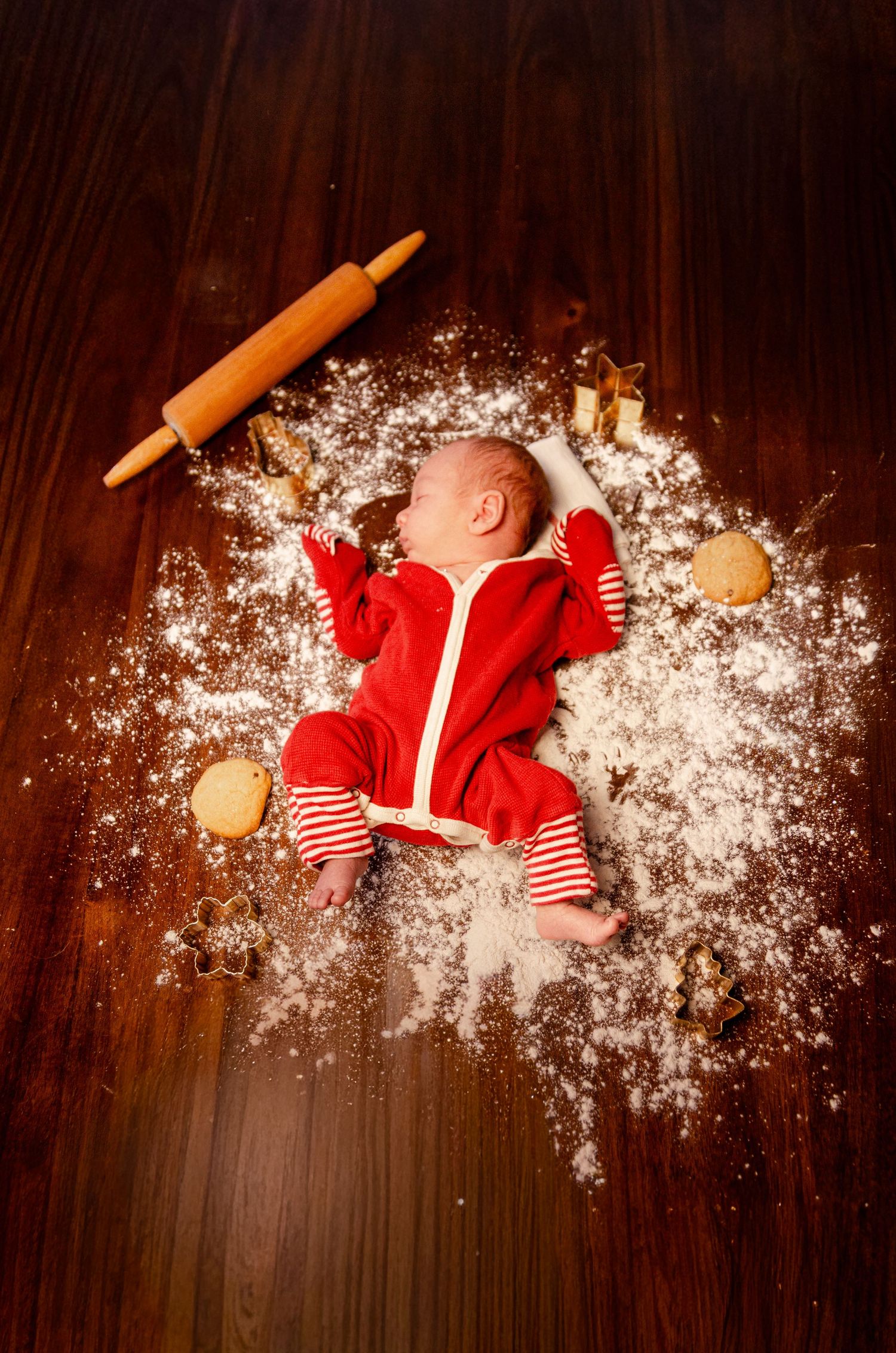 Baby in red outfit lying on wooden floor with baking flour and rolling pin. Newborn photography in Columbus, OH