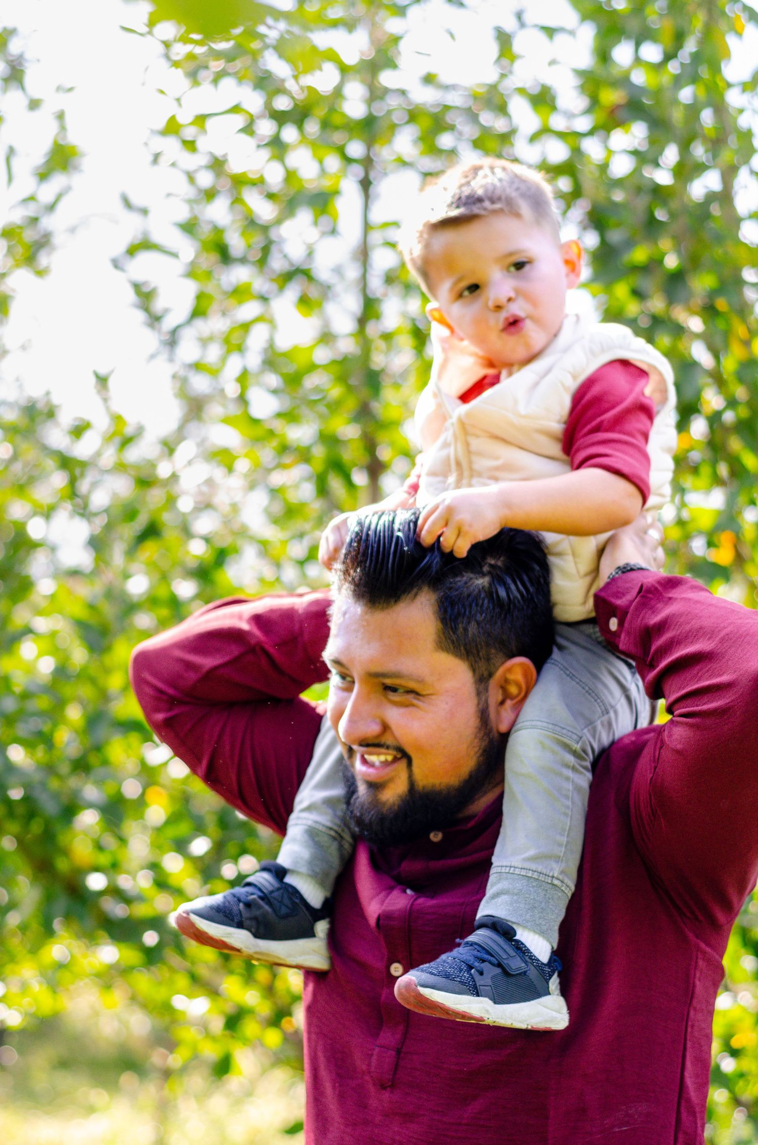 A playful moment captured outdoors with a toddler being held up high against a green leafy background. Photos by KM Conceptions Photography.