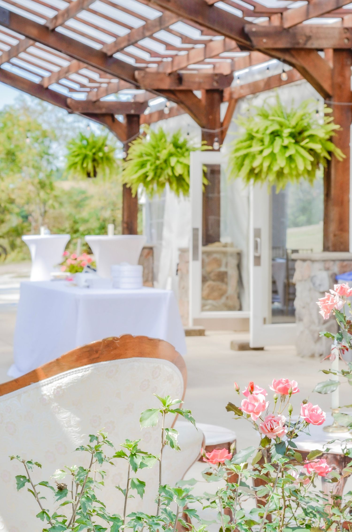 Elegant outdoor venue with white planters and pink roses under a wooden pergola. Wedding photos by KM Conceptions Photography.