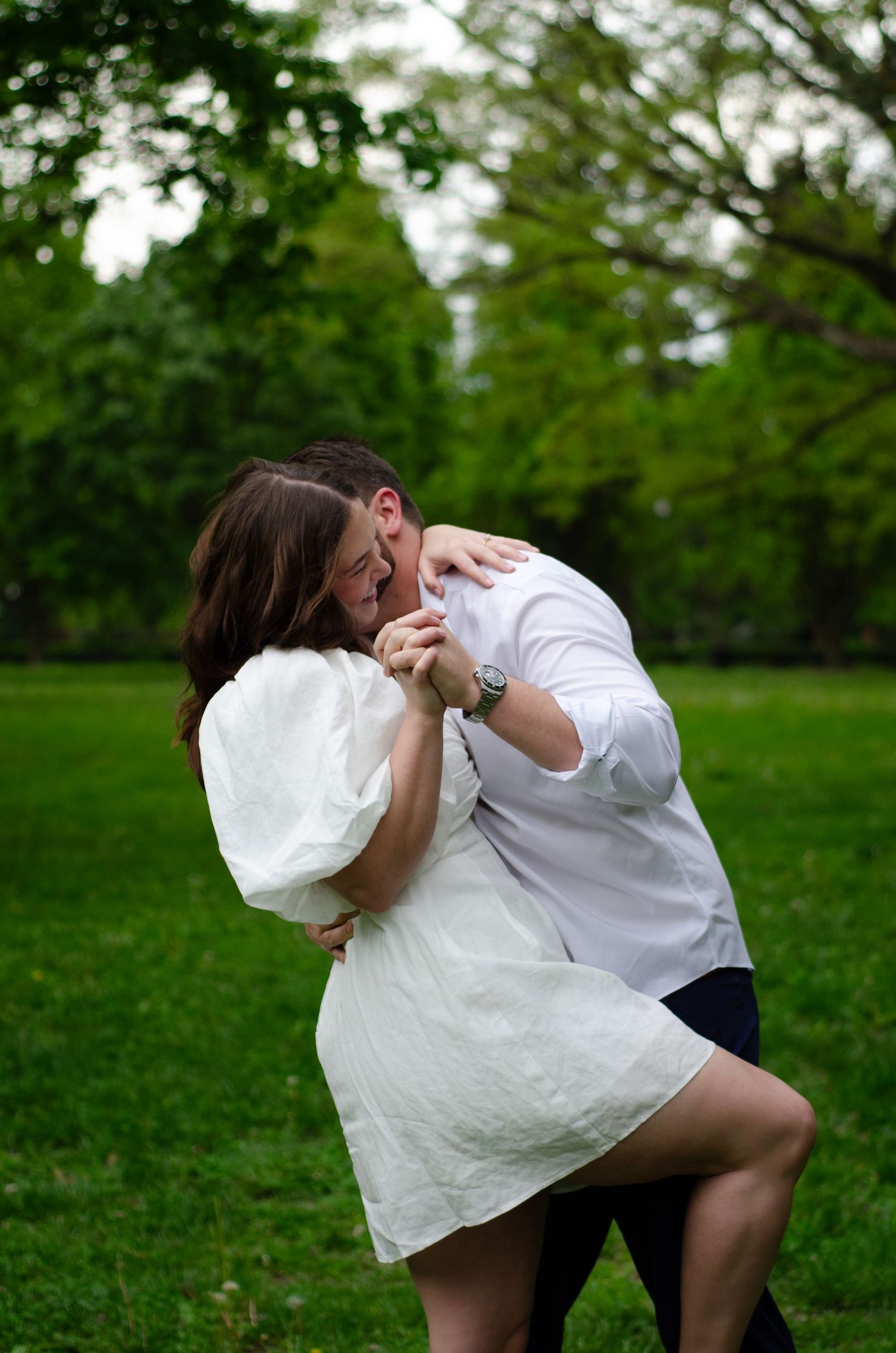 Couple in white clothing dancing and laughing together on green grass.