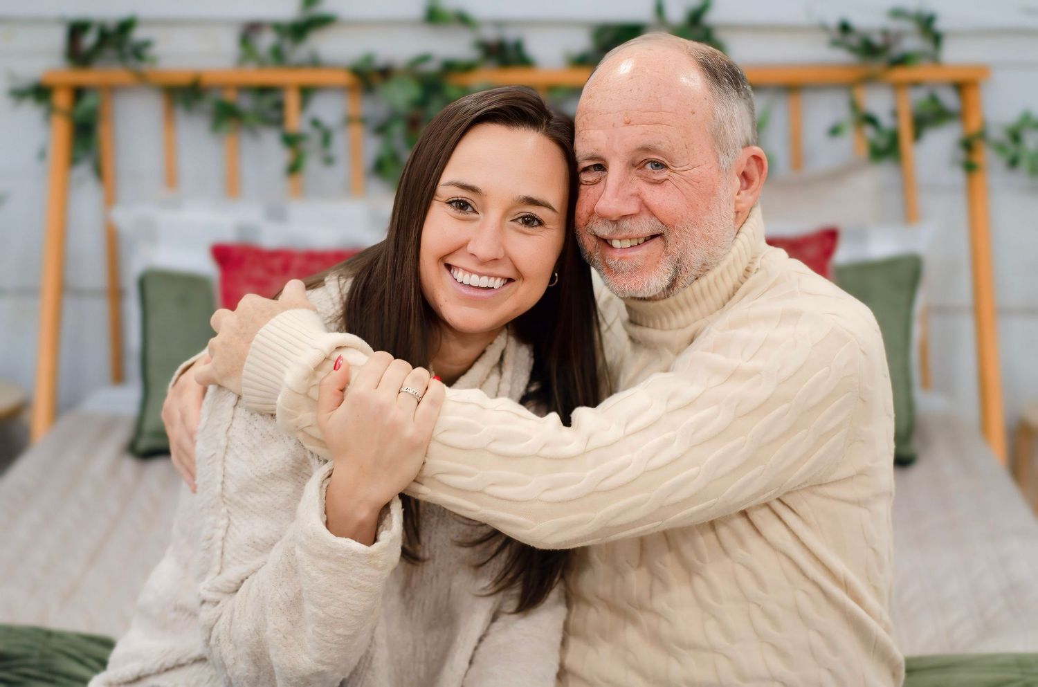 People embrace and smile together in front of decorative indoor backdrop.