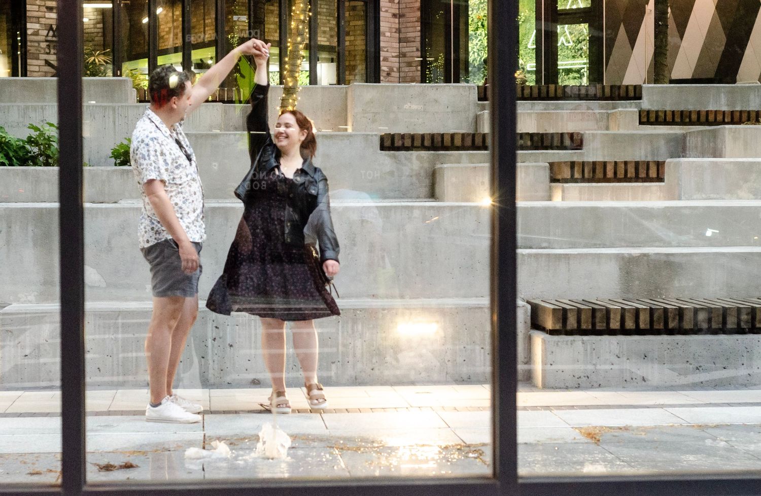 A couple dancing outdoors near concrete steps and lush greenery in an urban setting.