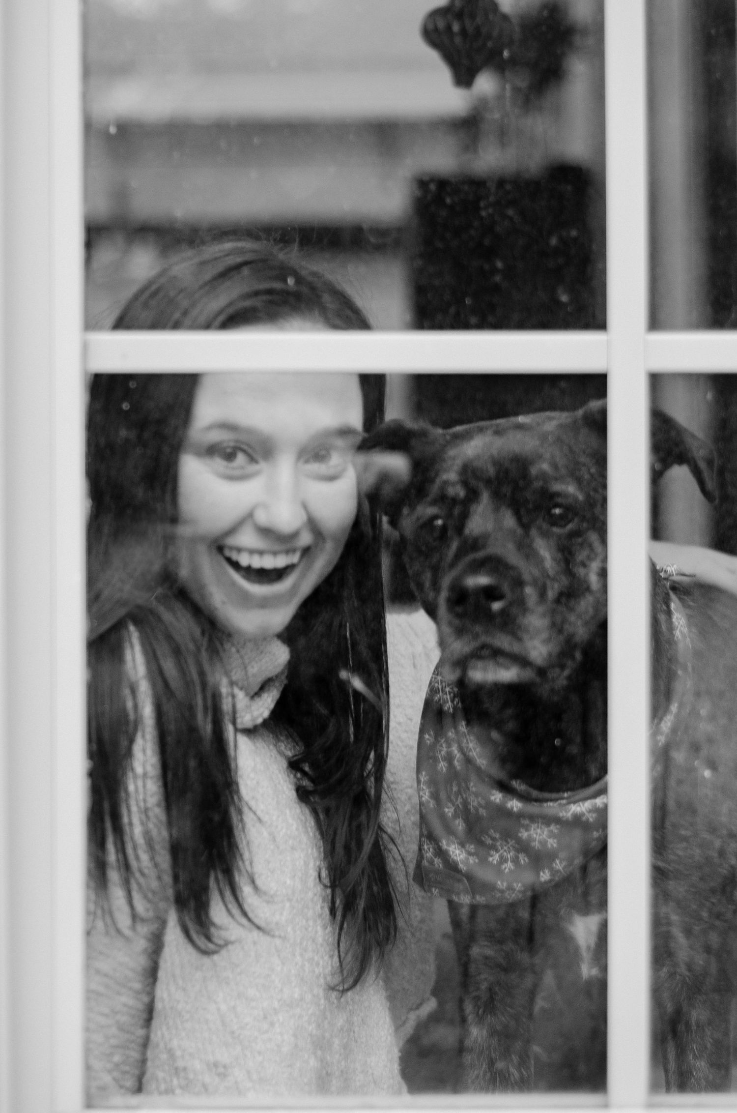 A joyful black and white photo through a window with a dark dog.