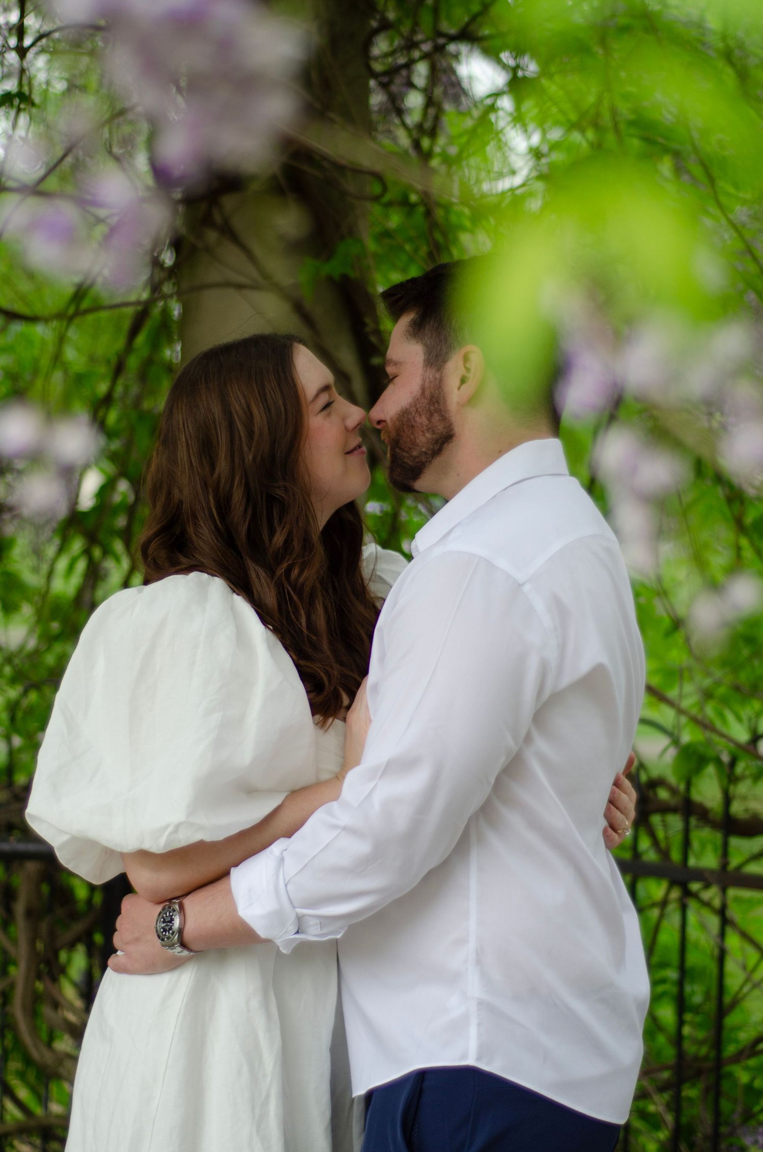 Romantic couple sharing a tender moment under flowering wisteria in a garden.