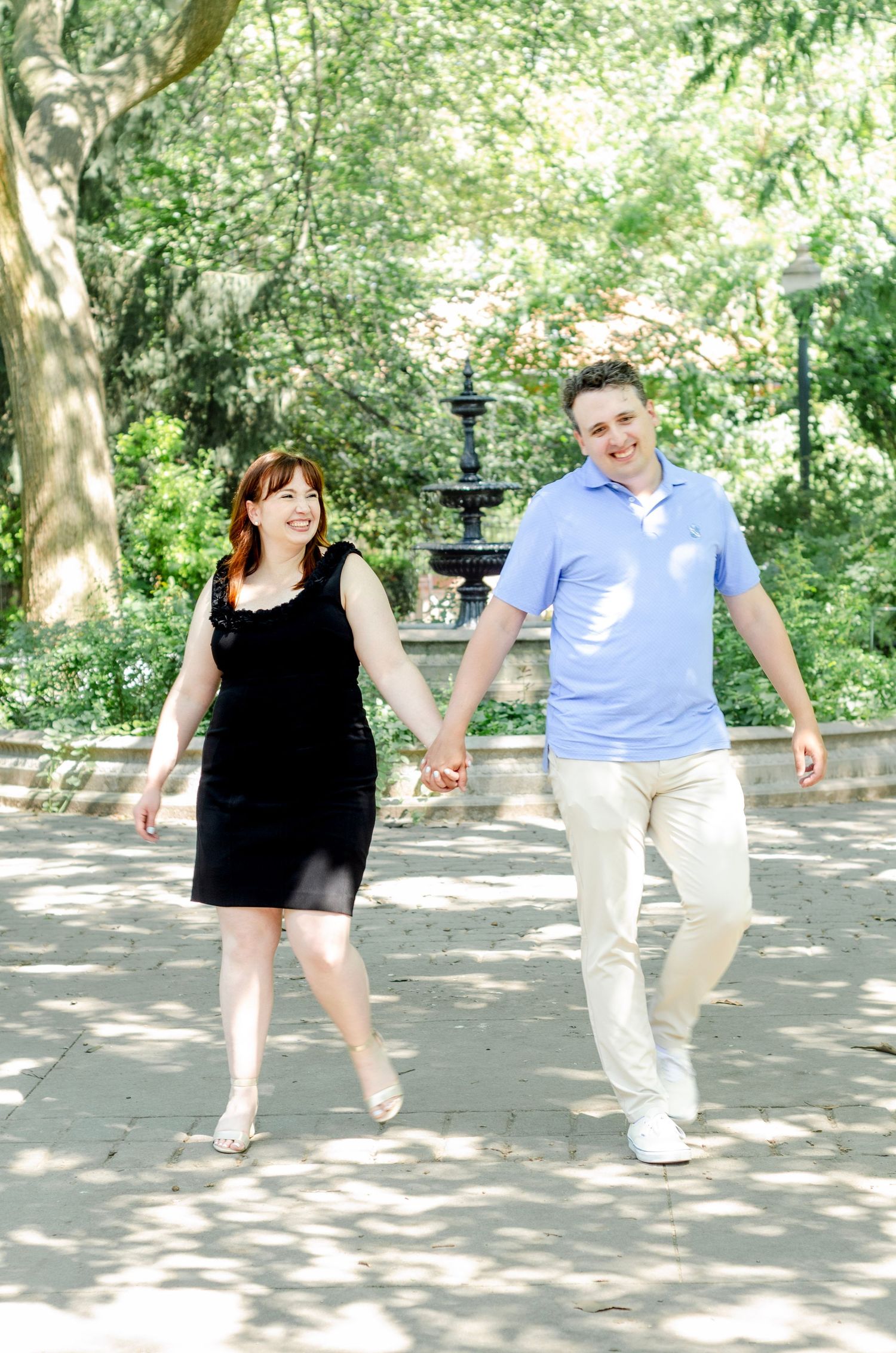 Playful couple dancing and laughing together in sunny park setting. Engagement photos by KM Conceptions Photography in New York.