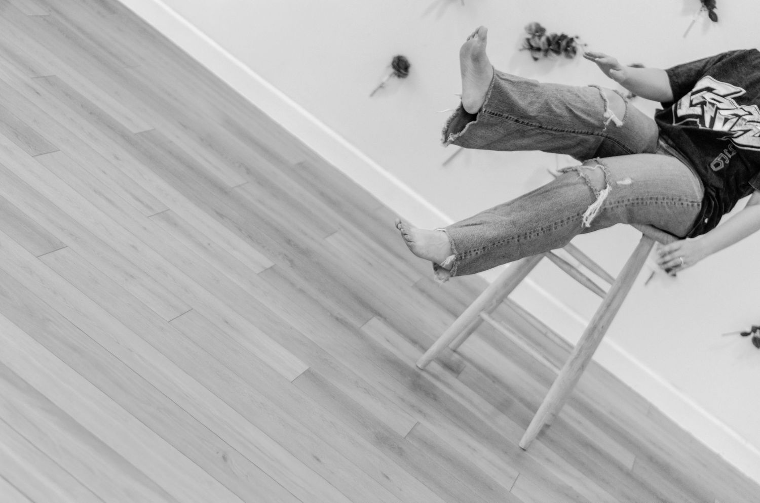 Black and white photo of a person lying on a wooden floor with legs resting on a white stool.