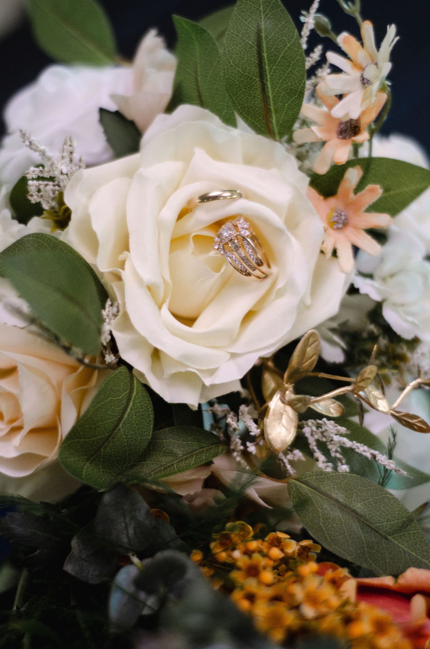 Elegant white roses and wedding rings displayed among green leaves and floral arrangements.