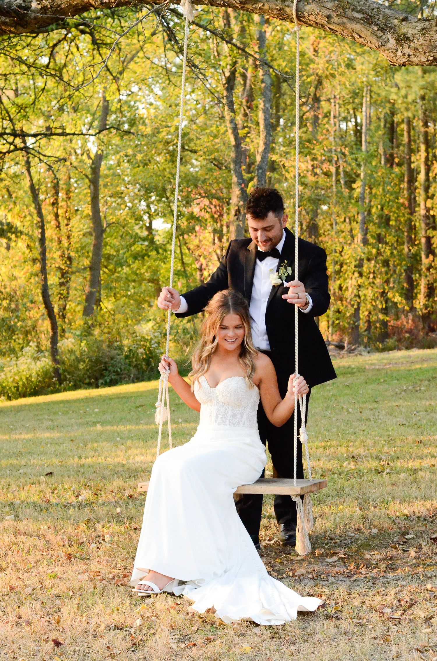 A couple on a tree swing shares romantic moments in a golden autumn forest setting during their wedding day. Photos by KM Conceptions.