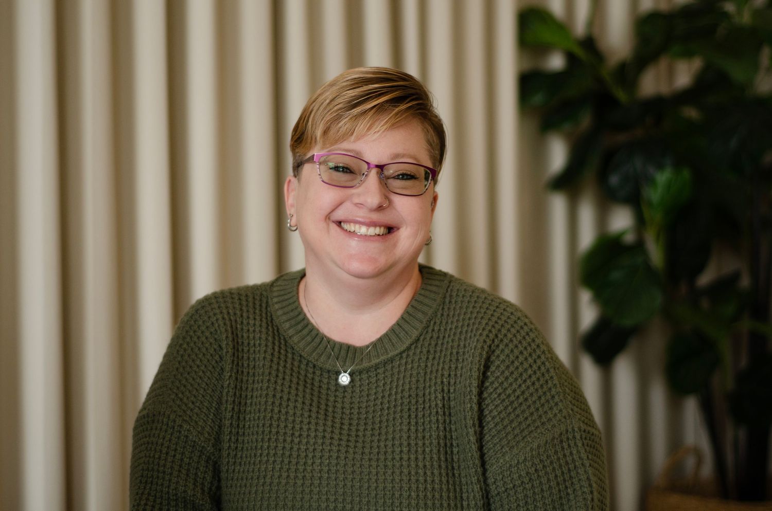 Professional headshot showing person in olive green sweater against neutral background.