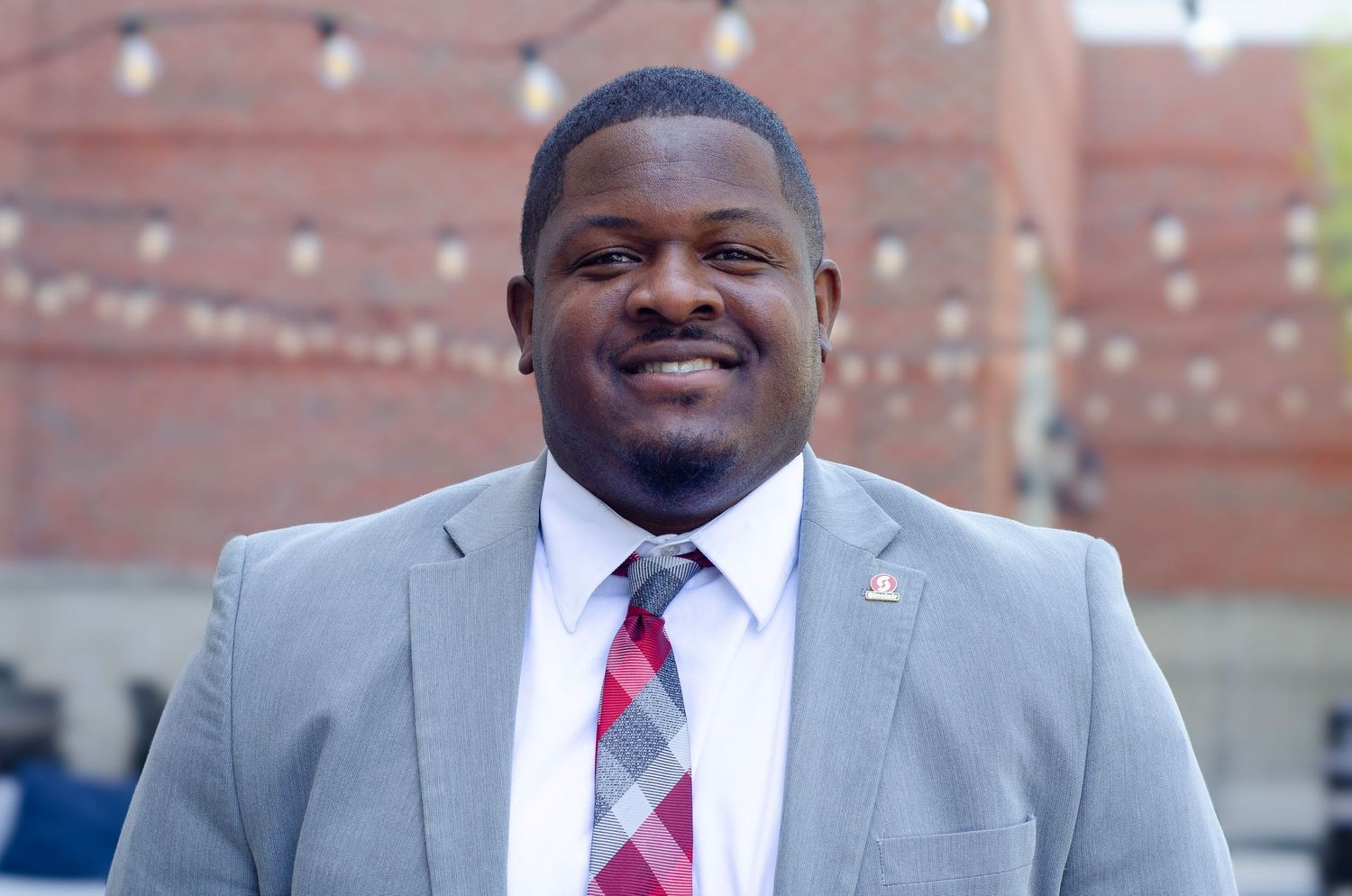 Professional headshots of person in grey suit and red tie against brick background.