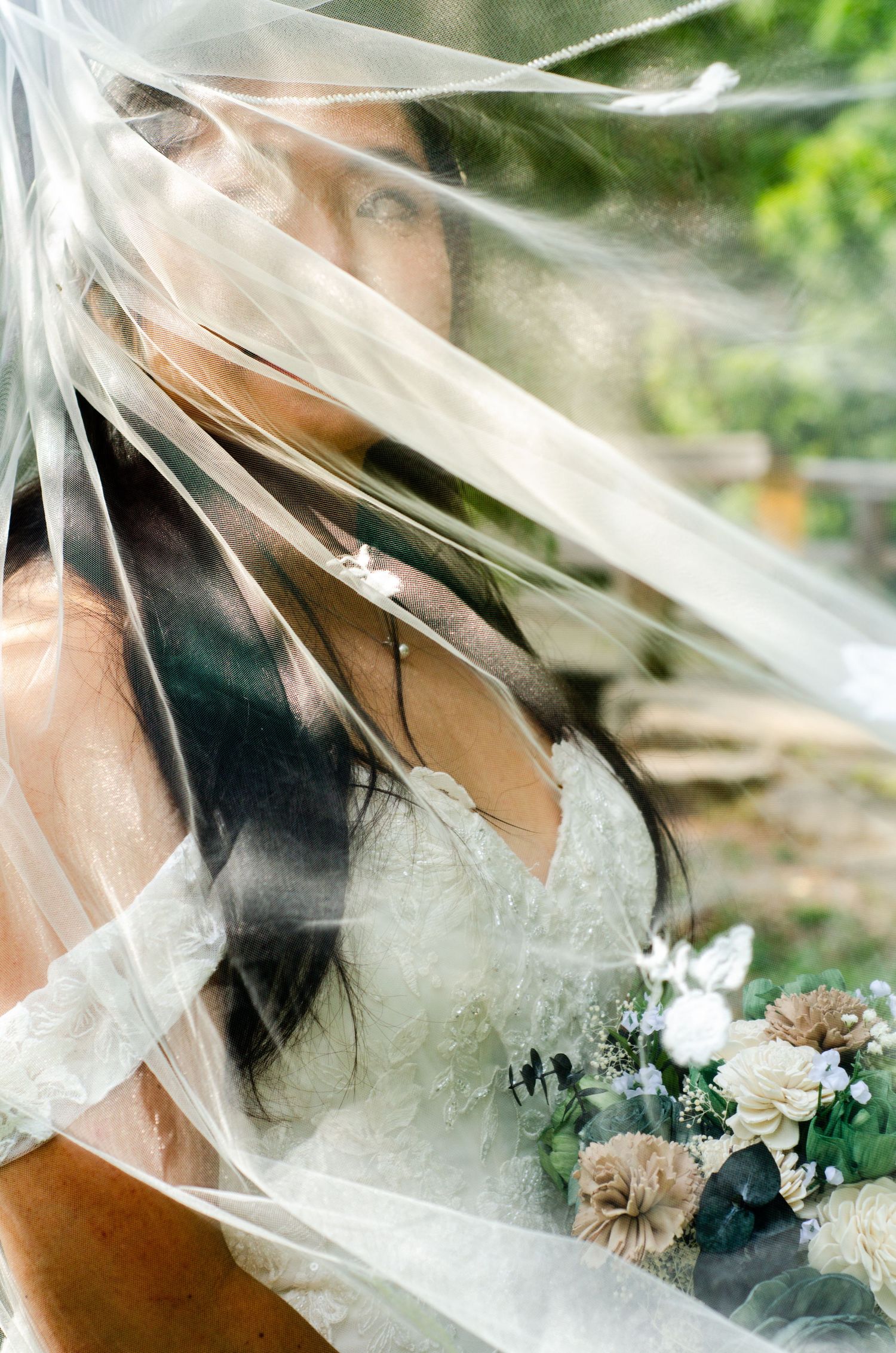 A delicate bridal veil catches the breeze in an artistic outdoor portrait among natural greenery.
