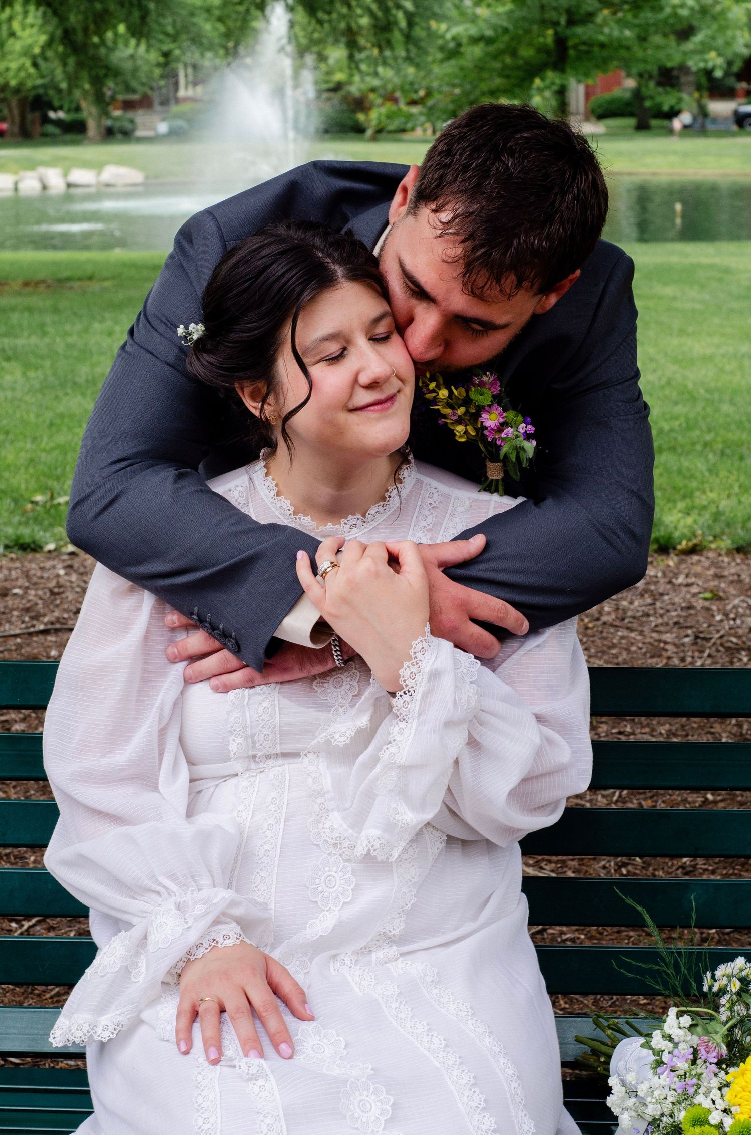 A tender romantic moment between a couple on a park bench with a fountain in the background. Wedding photos by KM Conceptions Photography.