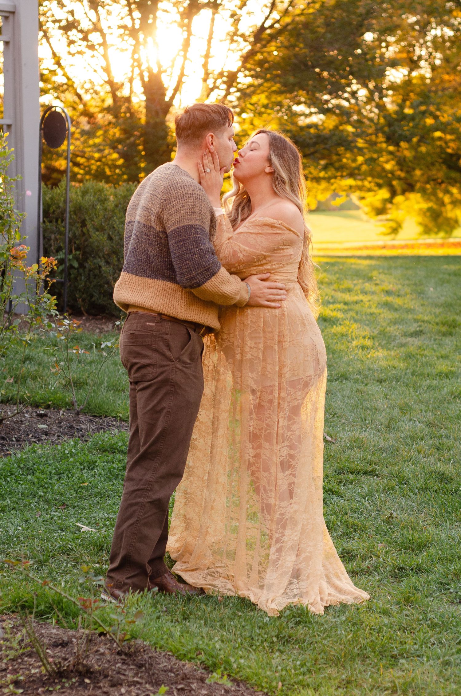 Couple embraces in a sunlit meadow wearing earth tones and lace. Maternity photos by KM Conceptions Photography in Columbus, OH.