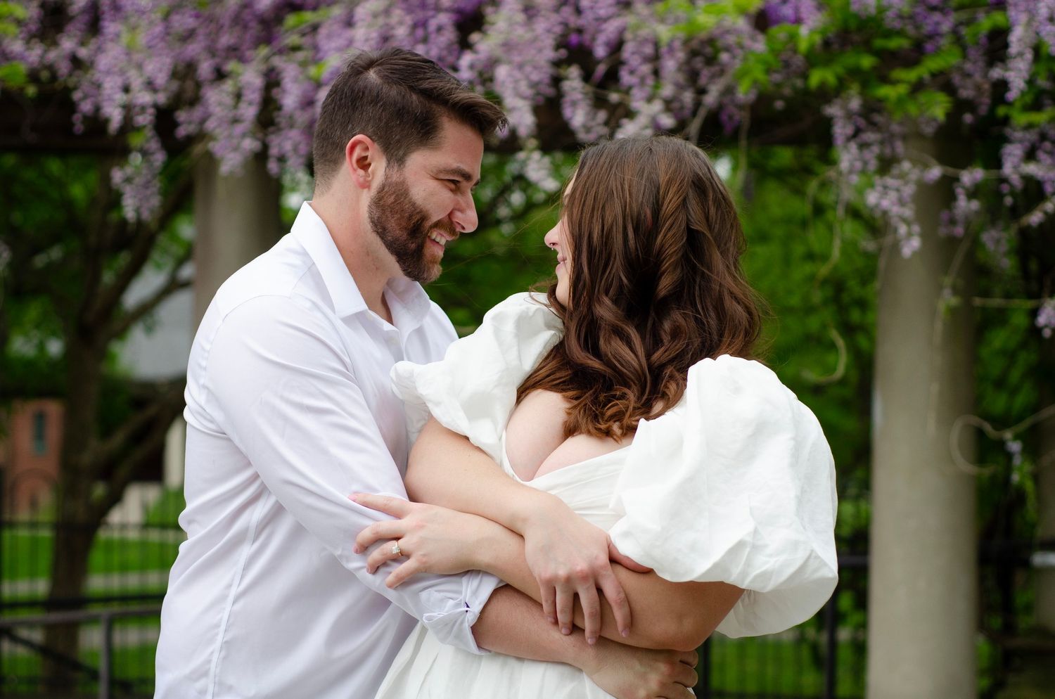 Couple laughing and embracing under flowering wisteria branches in springtime.