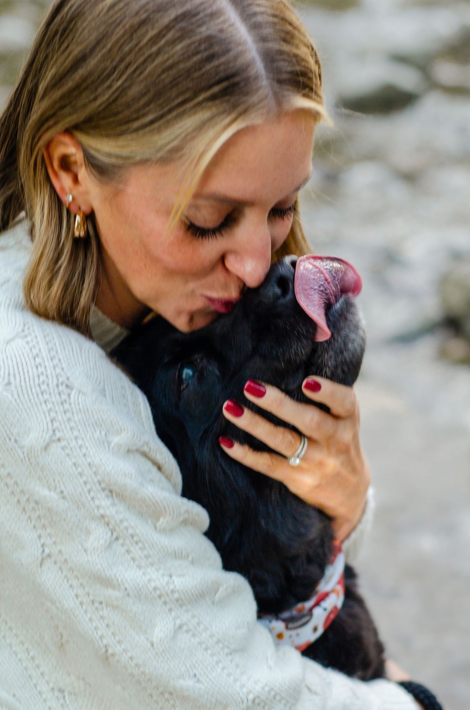 Person in white sweater hugging black dog with pink collar outdoors. Pet photos by KM Conceptions Photography in Columbus, OH.
