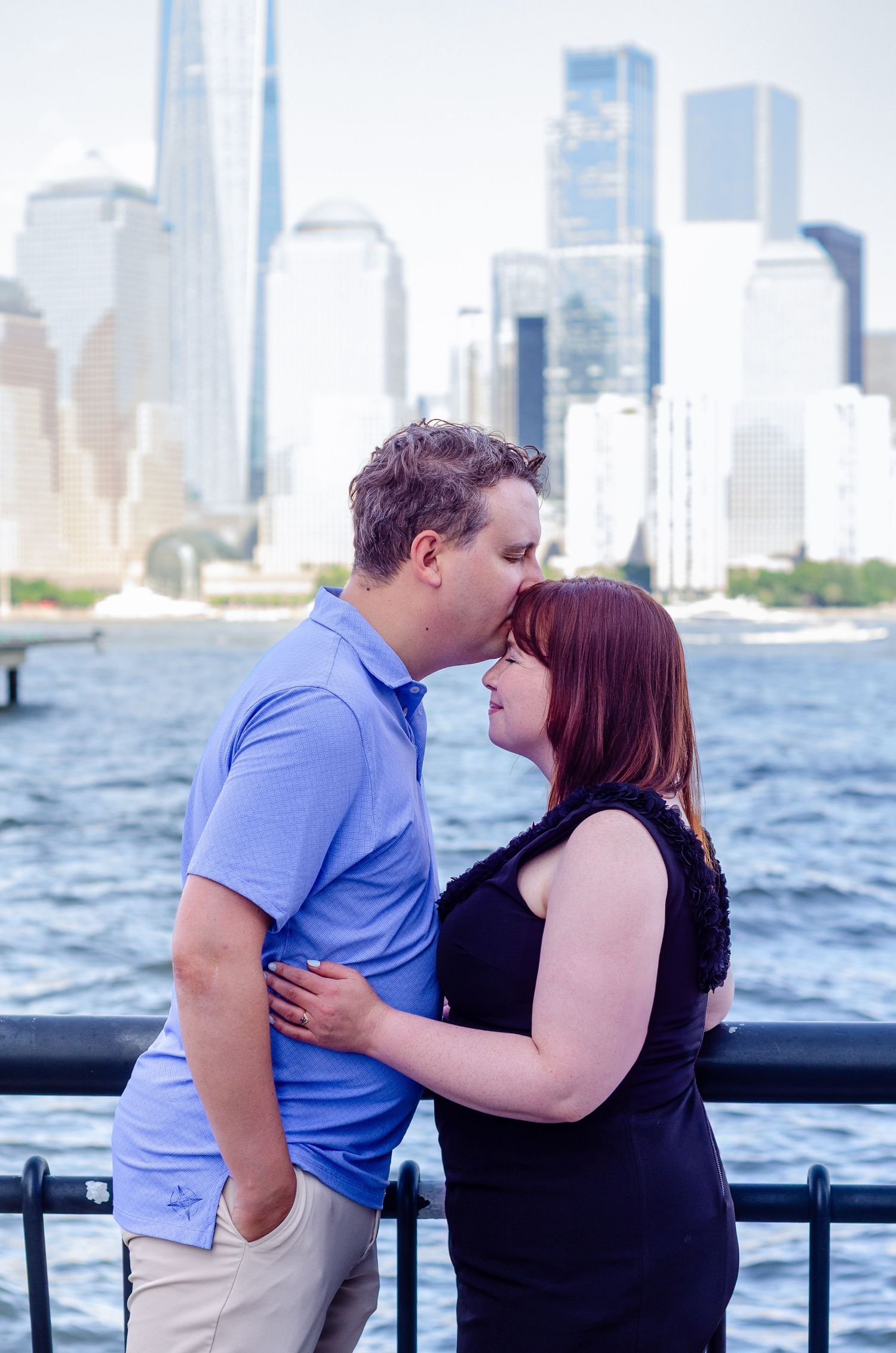 Couple sharing tender moment with Manhattan skyline visible across the water. Engagement photos by KM Conceptions Photography in New York.